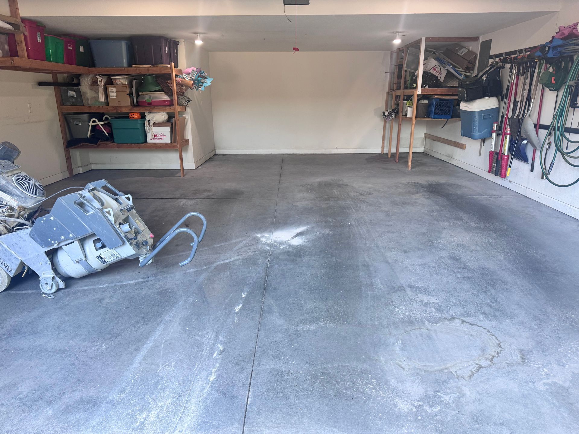Gray concrete garage with shelves, tools, and a floor grinder.