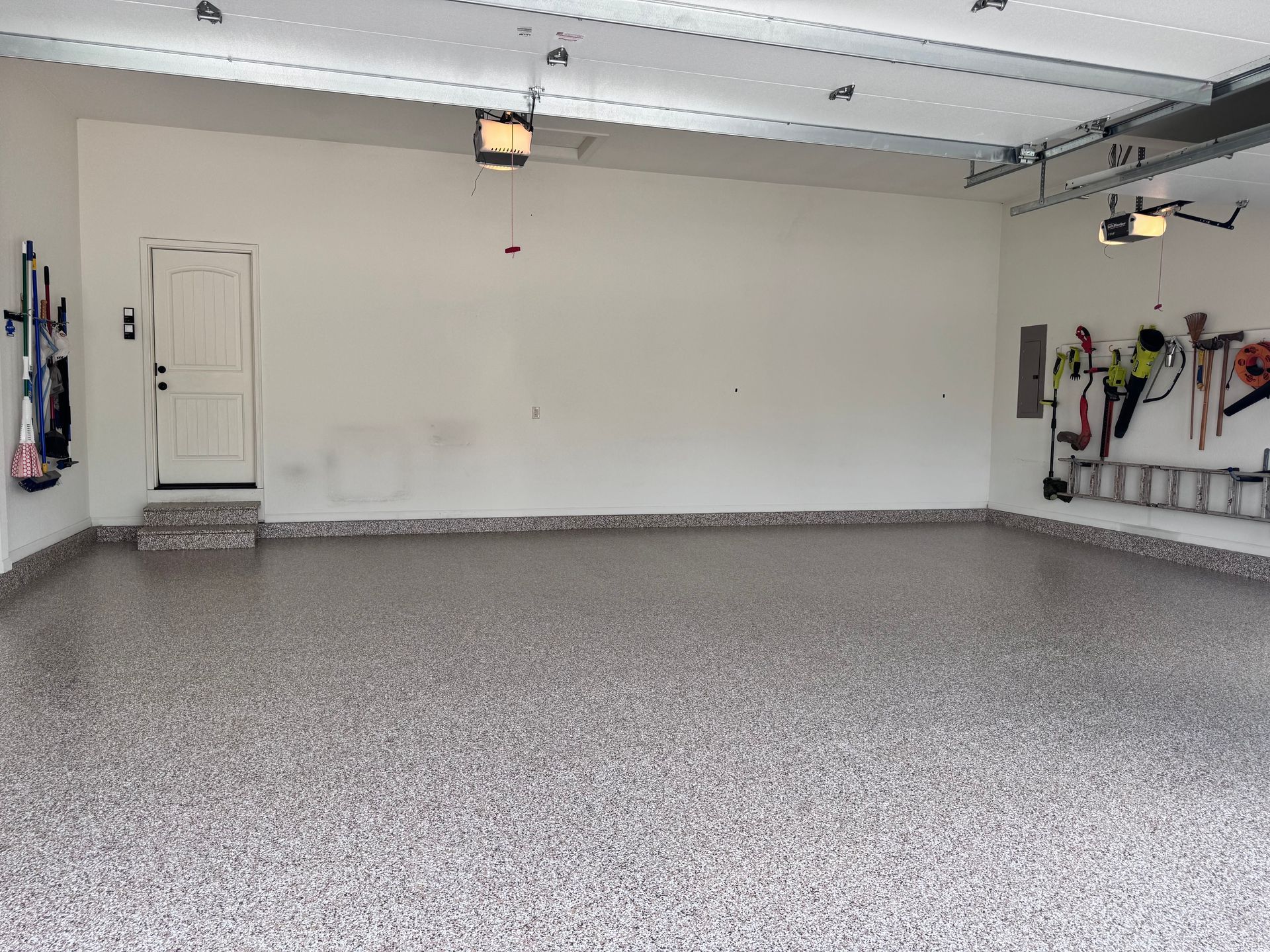 Empty garage with epoxy floor, white walls, and a door. Tools are hung on the left and right sides.