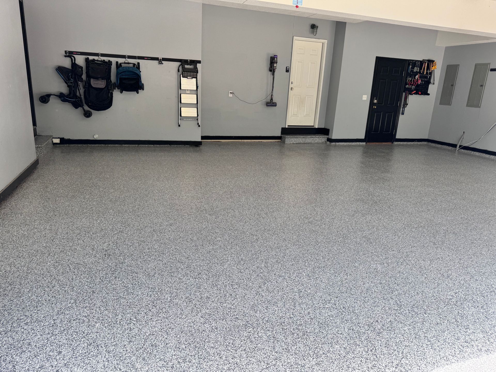 Gray epoxy-coated garage floor. Gray walls, dark trim. Tools on the wall, two doors in background.
