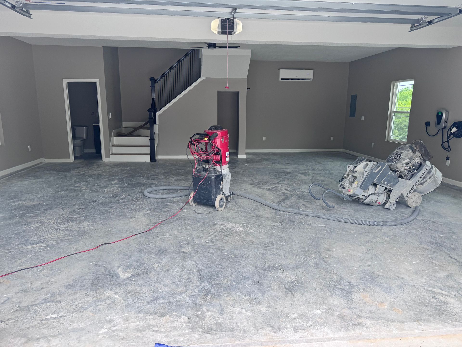 Garage interior with concrete floor, construction equipment, stairs, and neutral-colored walls.