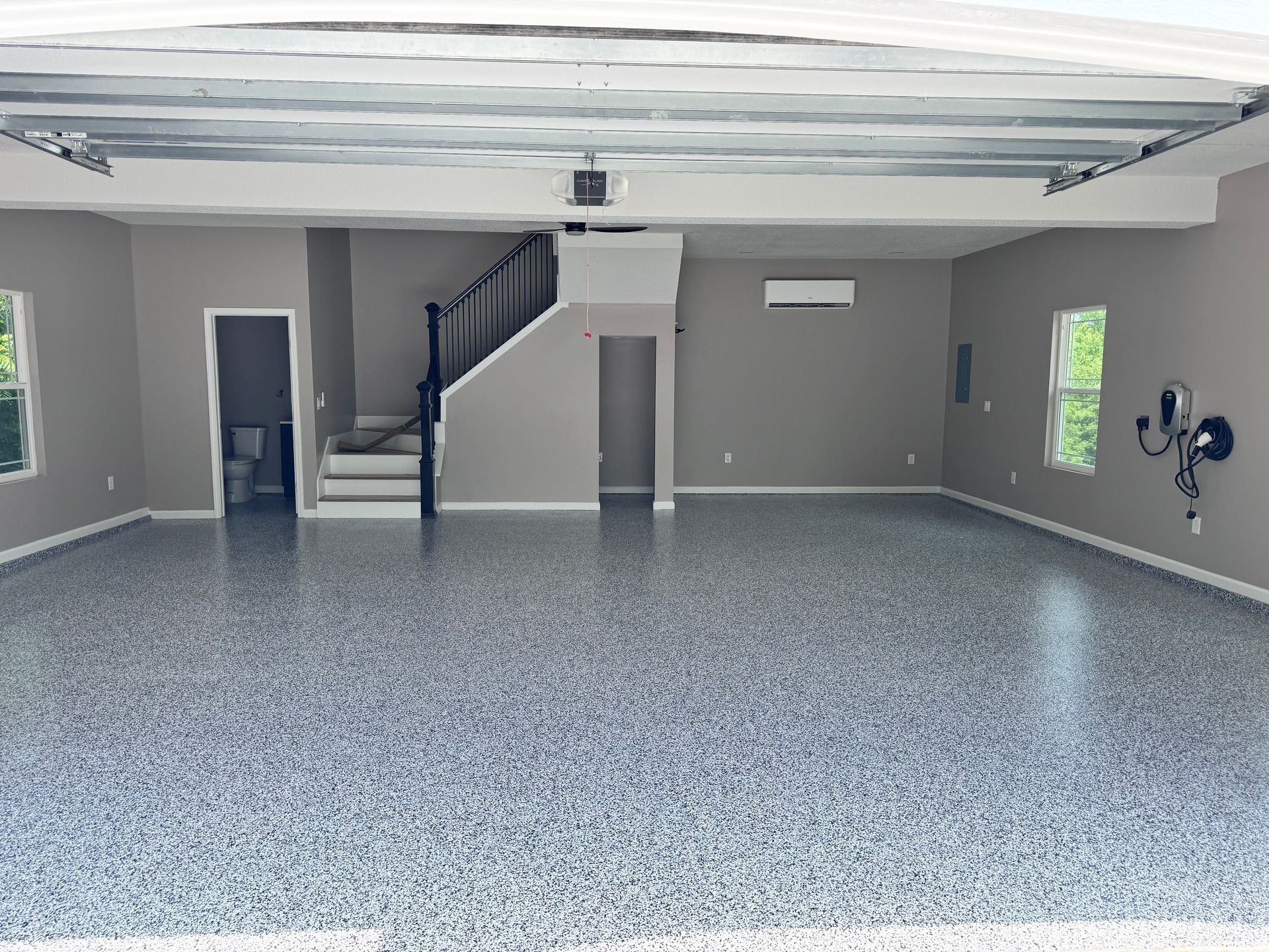 Spacious, empty garage with epoxy floor, stairs, and a door, painted in neutral colors.