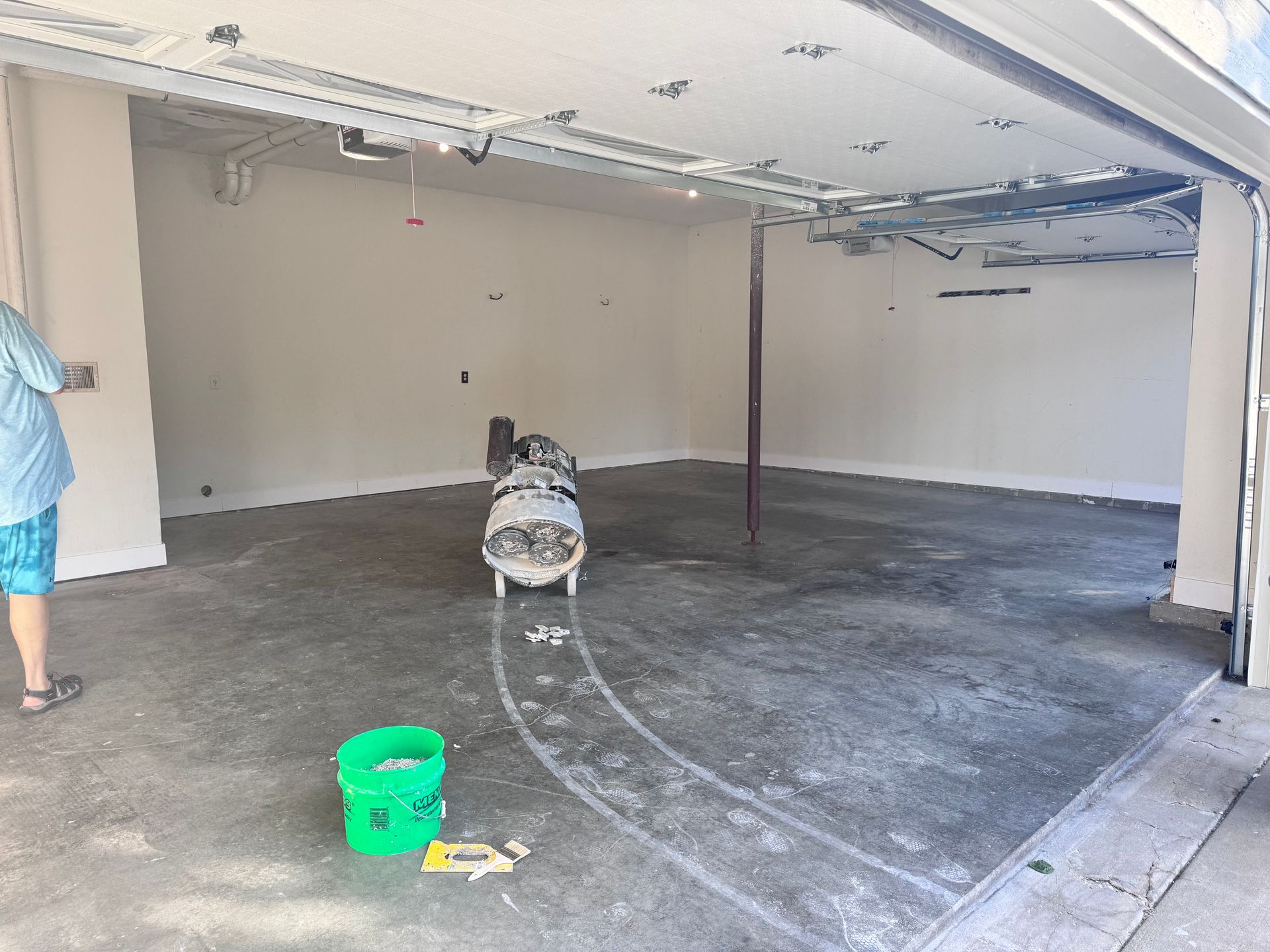 Empty garage with a gray concrete floor, open door, and an air compressor.