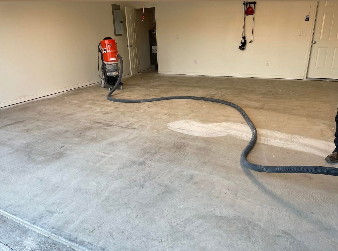 Concrete floor being prepared with a vacuum and hose in a garage.