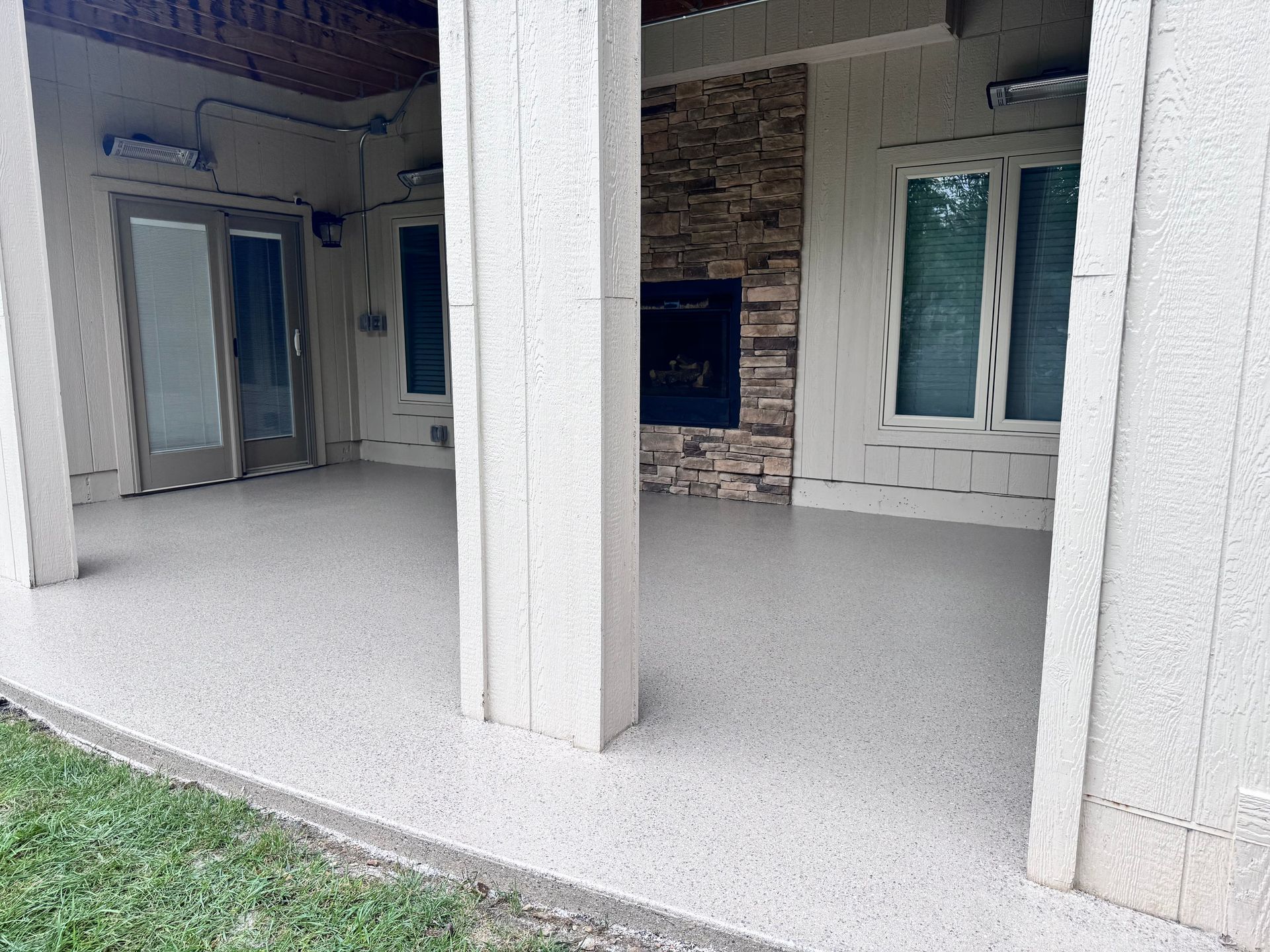 Covered patio with light-colored flooring, columns, a fireplace, and glass doors.