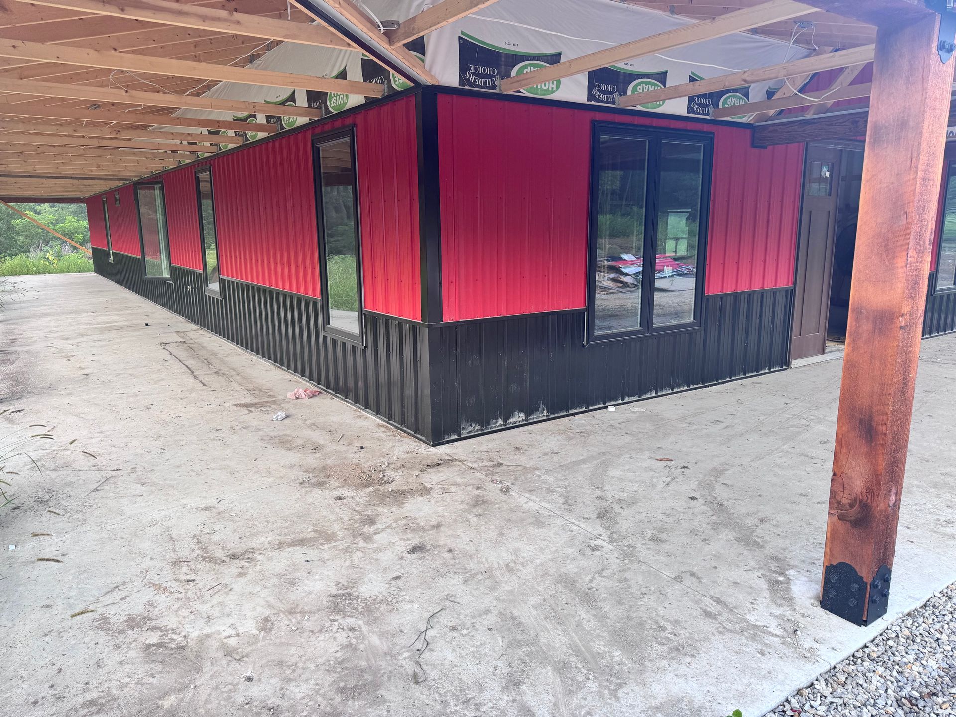 Red and black building with multiple windows under a wooden roof.