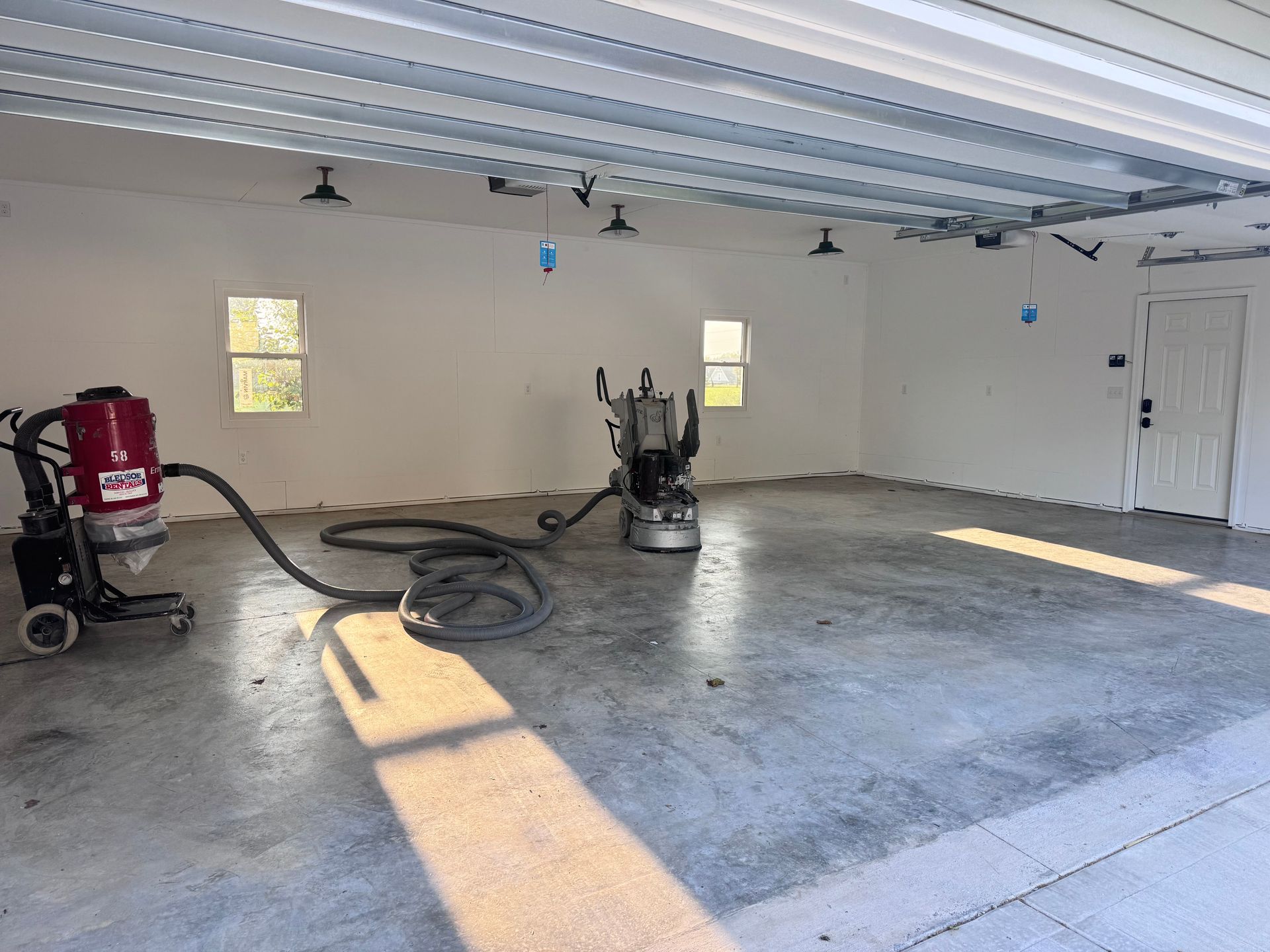 Garage interior during floor grinding, with two machines and overhead lighting.
