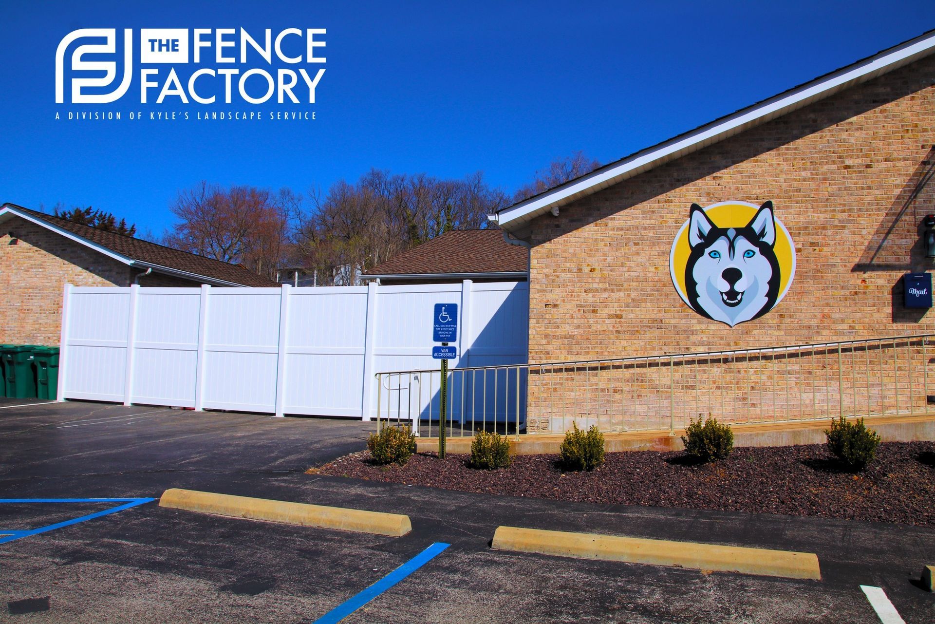 White fence in front of a brick building with a Husky logo and a blue handicap parking spot.