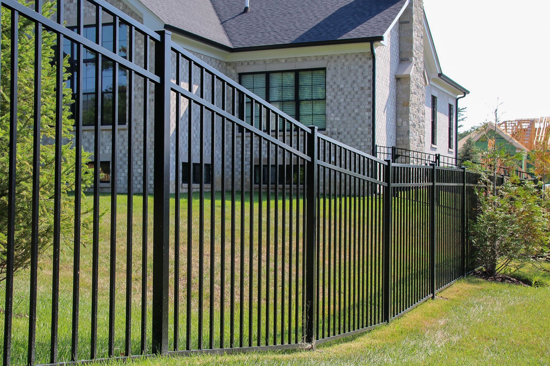 Black metal fence surrounding a light-colored brick house on a grassy lawn.