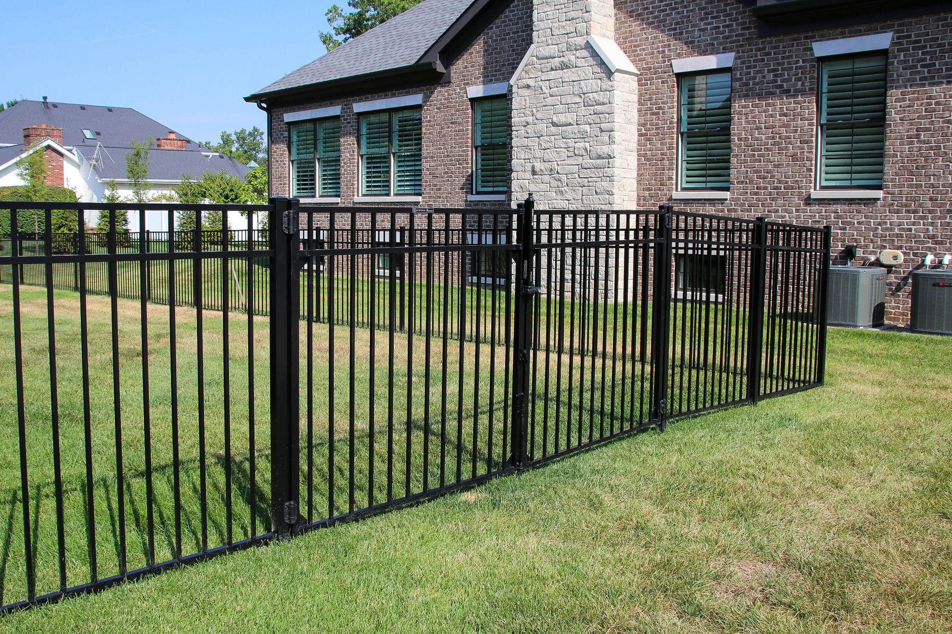 Black metal fence surrounding a grassy backyard next to a brick house.