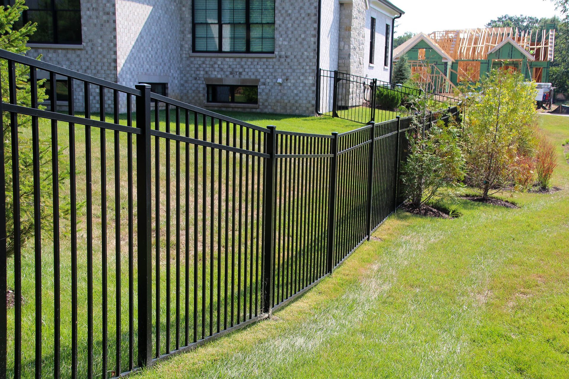 Black metal fence in front of a brick house with a green lawn.