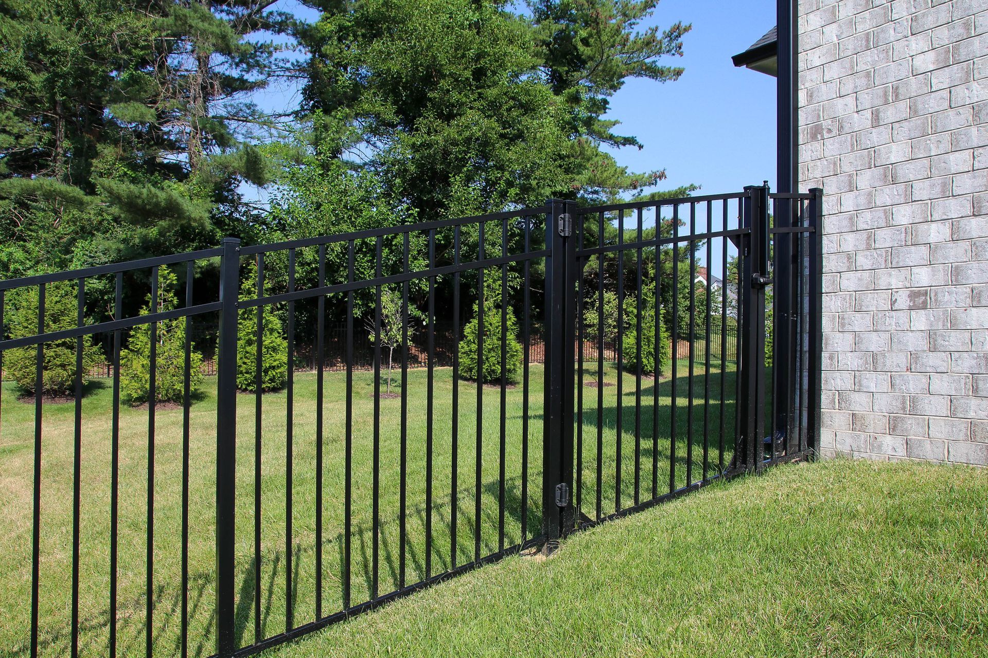 Black metal fence with gate beside a brick wall, on a grassy lawn.