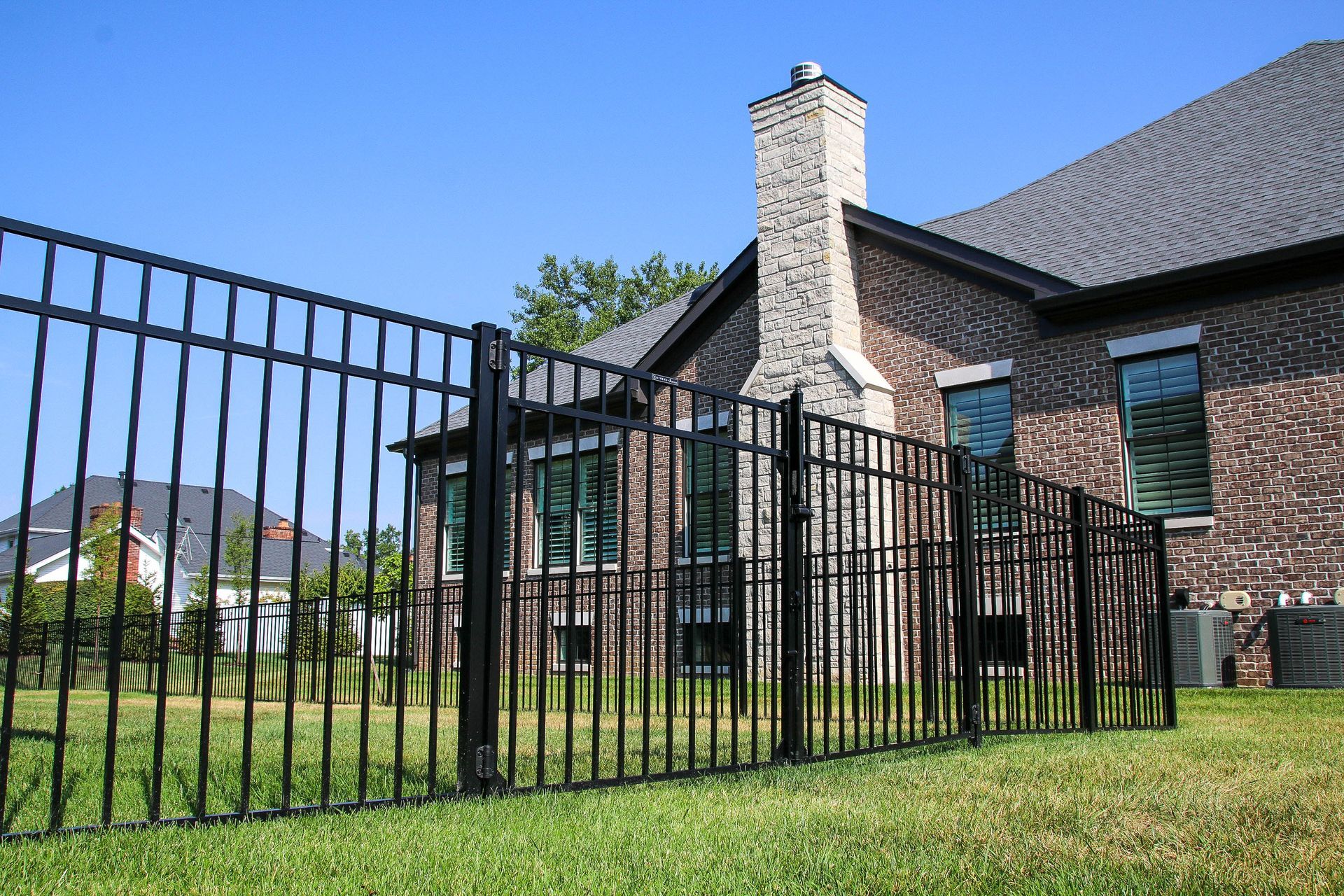 Black metal fence in front of a brick house with a chimney and blue sky.