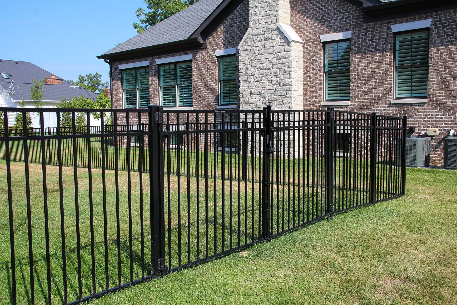 Black metal fence in front of a brick building with windows. Green grass surrounds the fence.