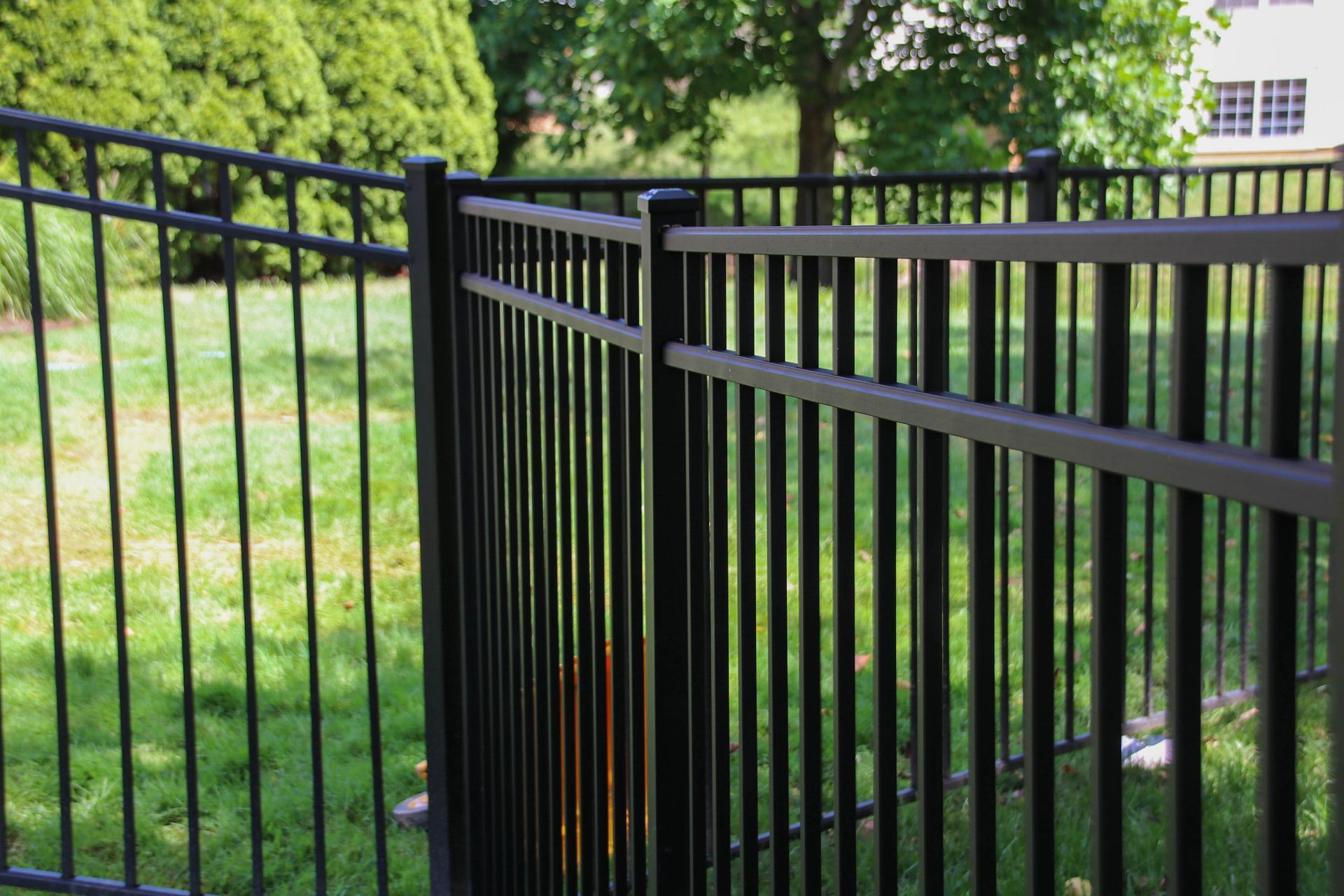 Black metal fence in a grassy yard, with vertical bars and horizontal rails.