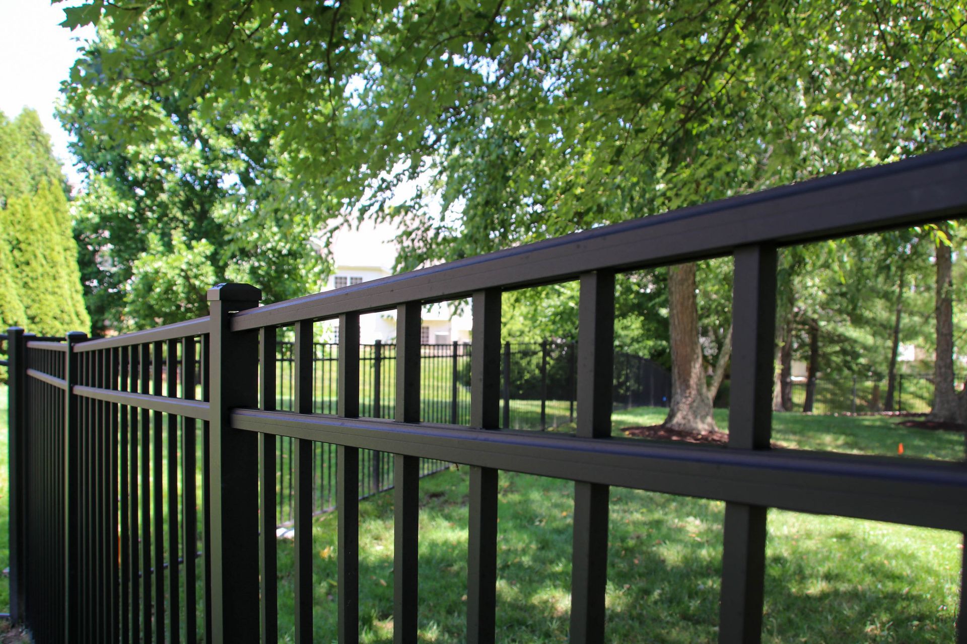 Black metal fence in a yard with trees and green grass.