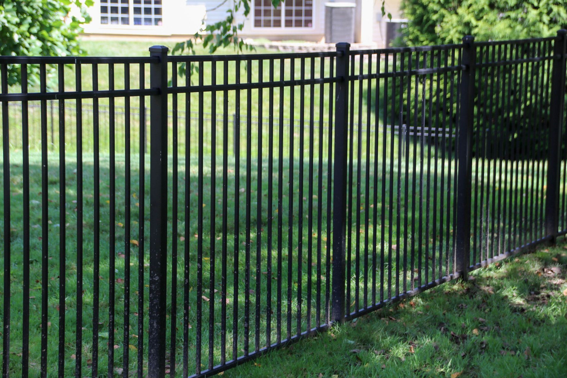 Black metal fence surrounding a grassy yard with a house visible in the background.