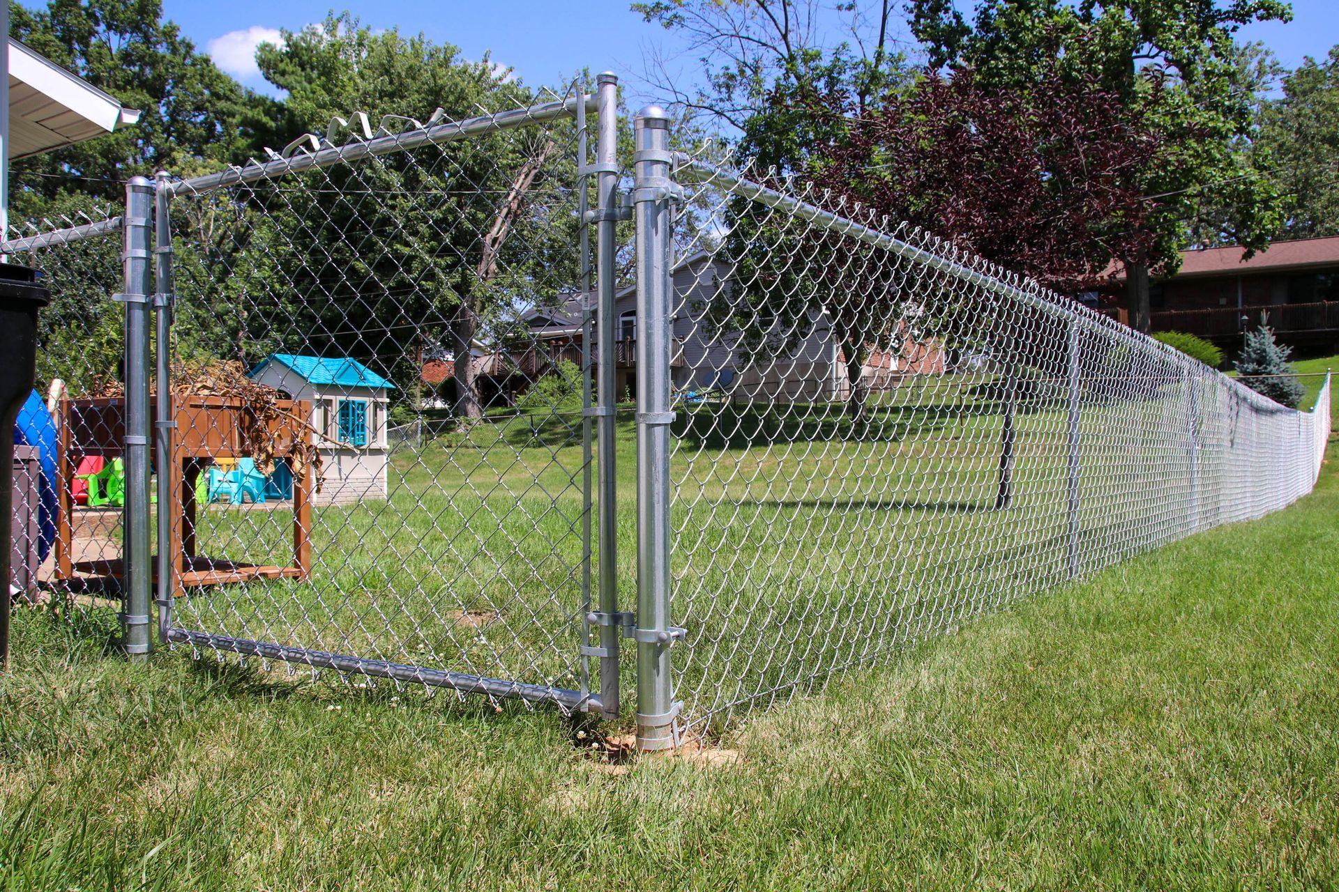 Chain-link fence in a grassy yard, partially enclosing the property, with a playhouse visible.