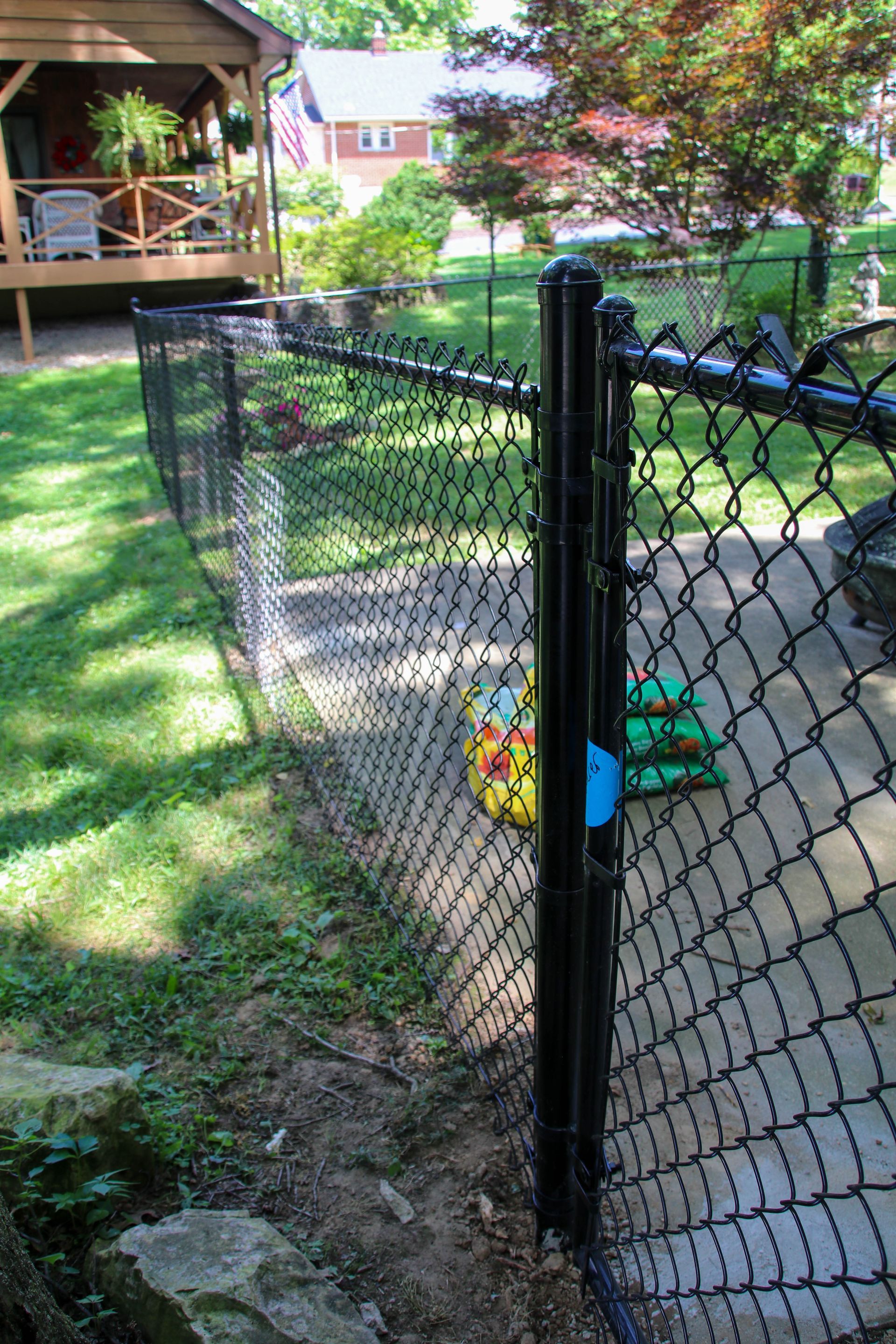 Black chain-link fence bordering a grassy yard, with a black post in the foreground.