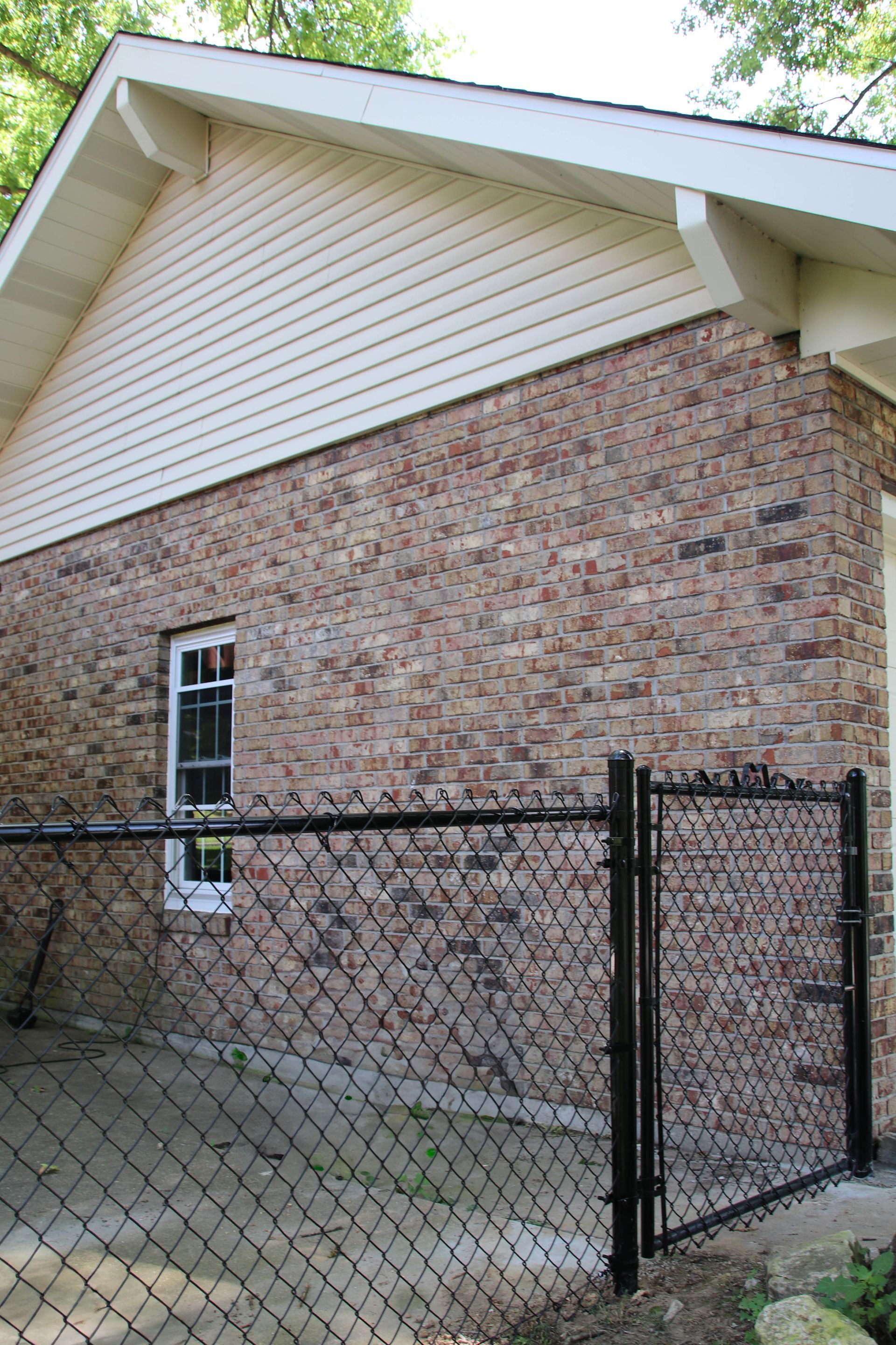 Brick building exterior with white trim, a small window, and a black chain-link fence.
