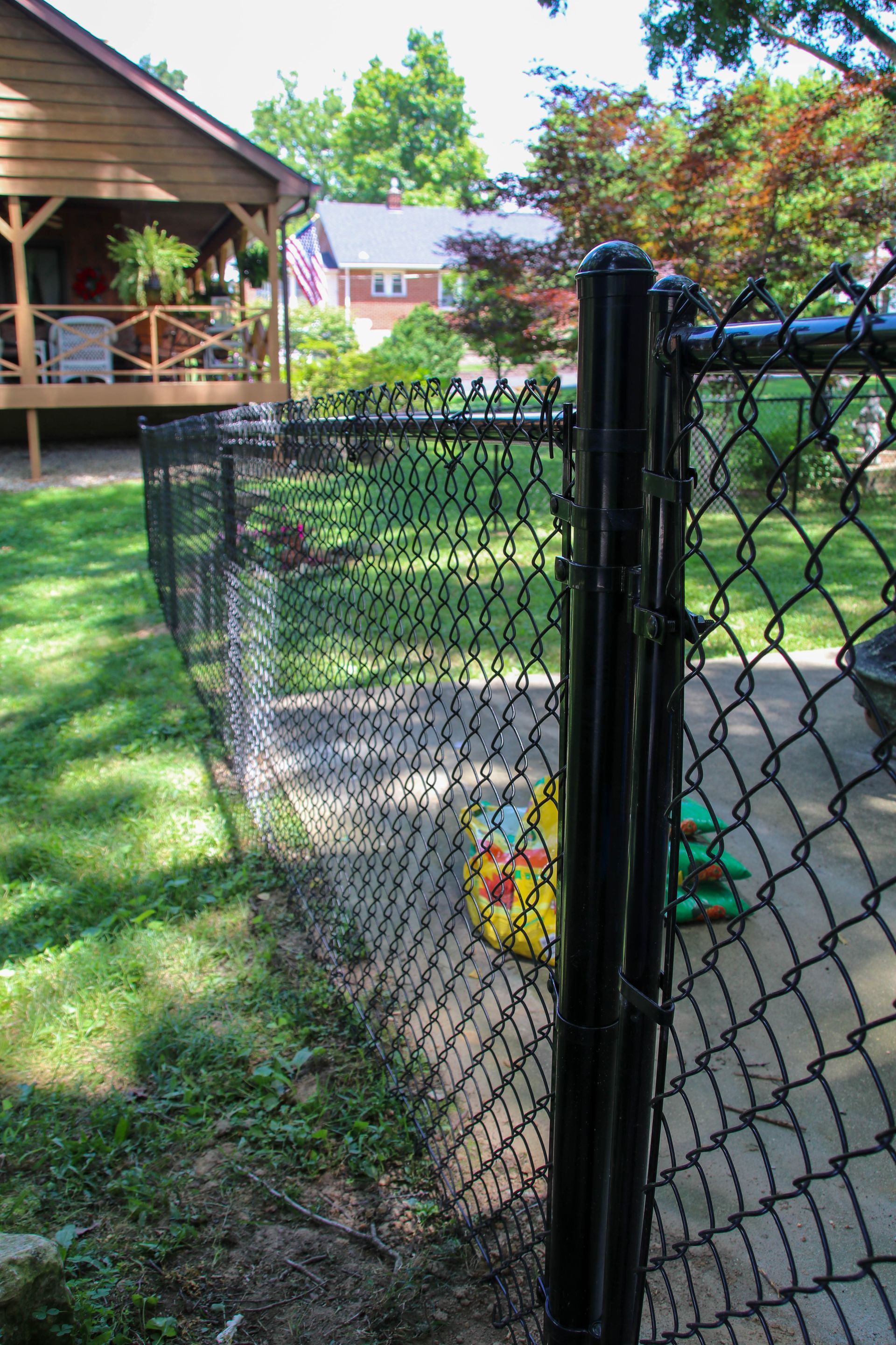 Black chain link fence in a backyard setting, next to a house with a porch.