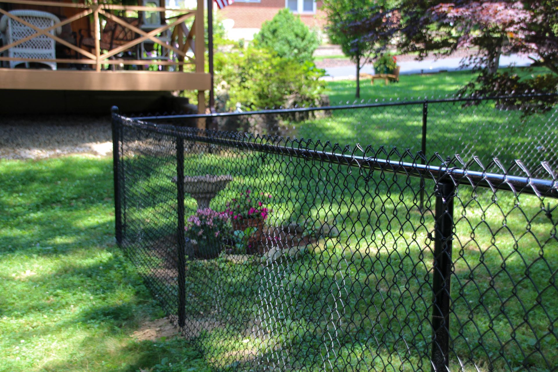 Black chain-link fence bordering a grassy backyard, with a deck and garden in the background.