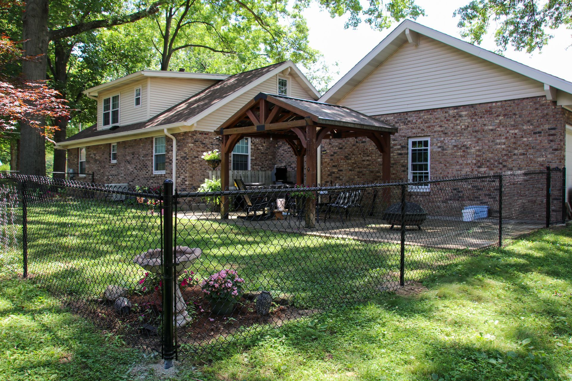 A brick house with a wooden pergola, fenced in yard, and chain link fence.