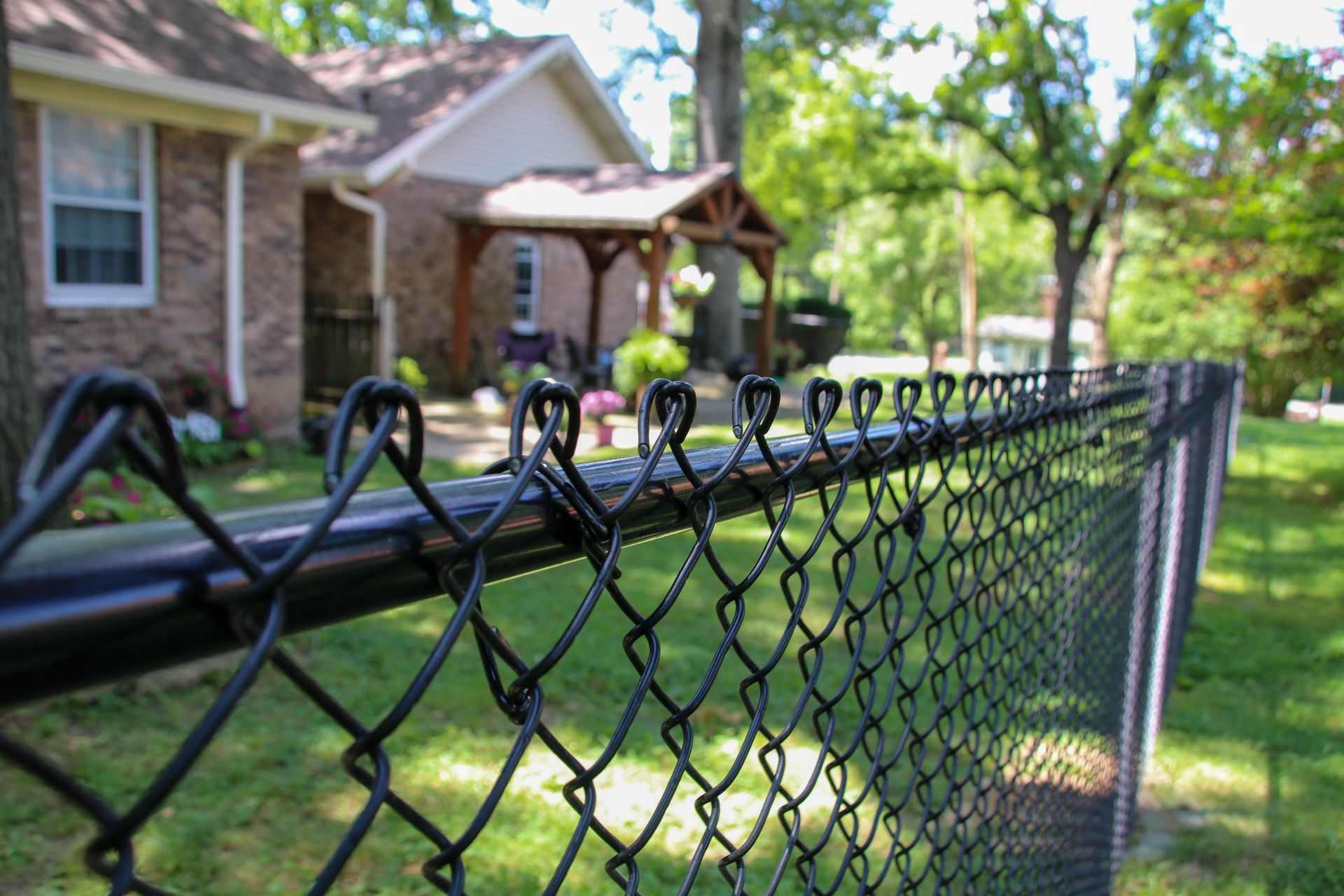 Black chain link fence in focus, with a brick house and yard in the background.