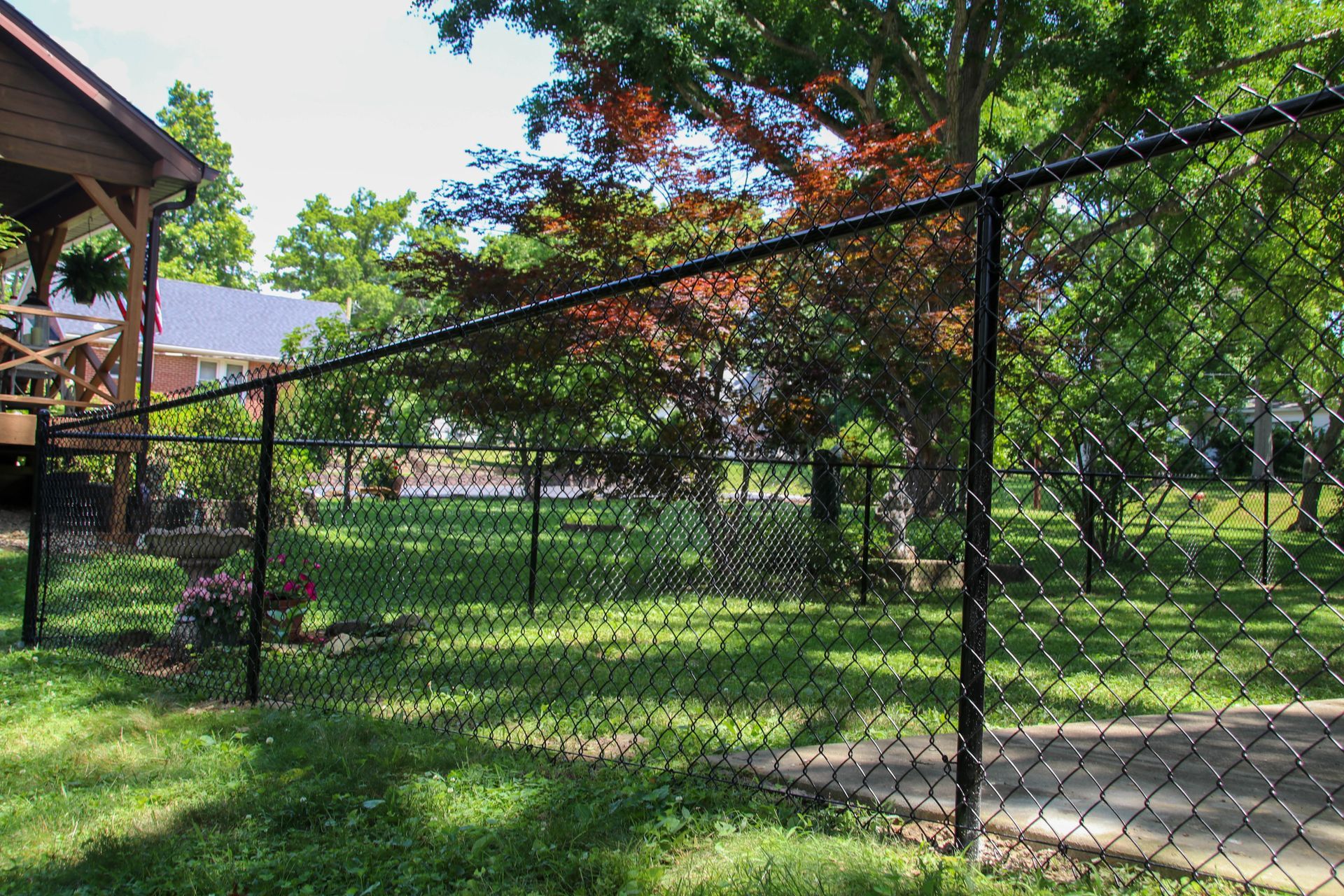 Black chain-link fence in a grassy yard, with trees and a house in the background.