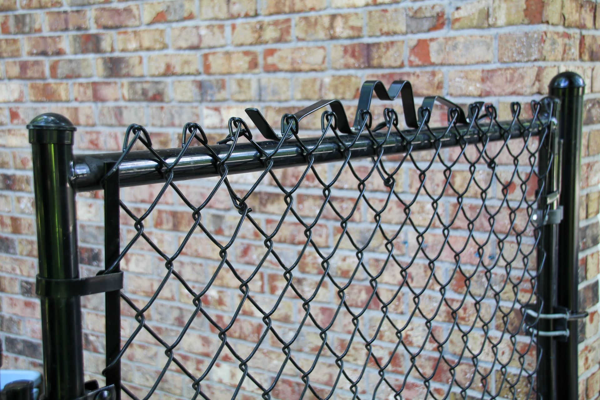 Black chain-link fence gate with decorative top against a brick wall.