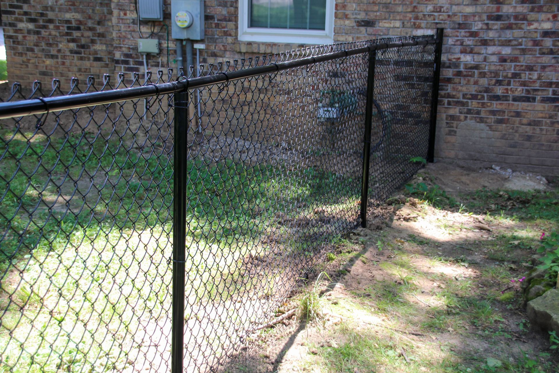 Black chain-link fence along a brick building, with a grassy area in front.