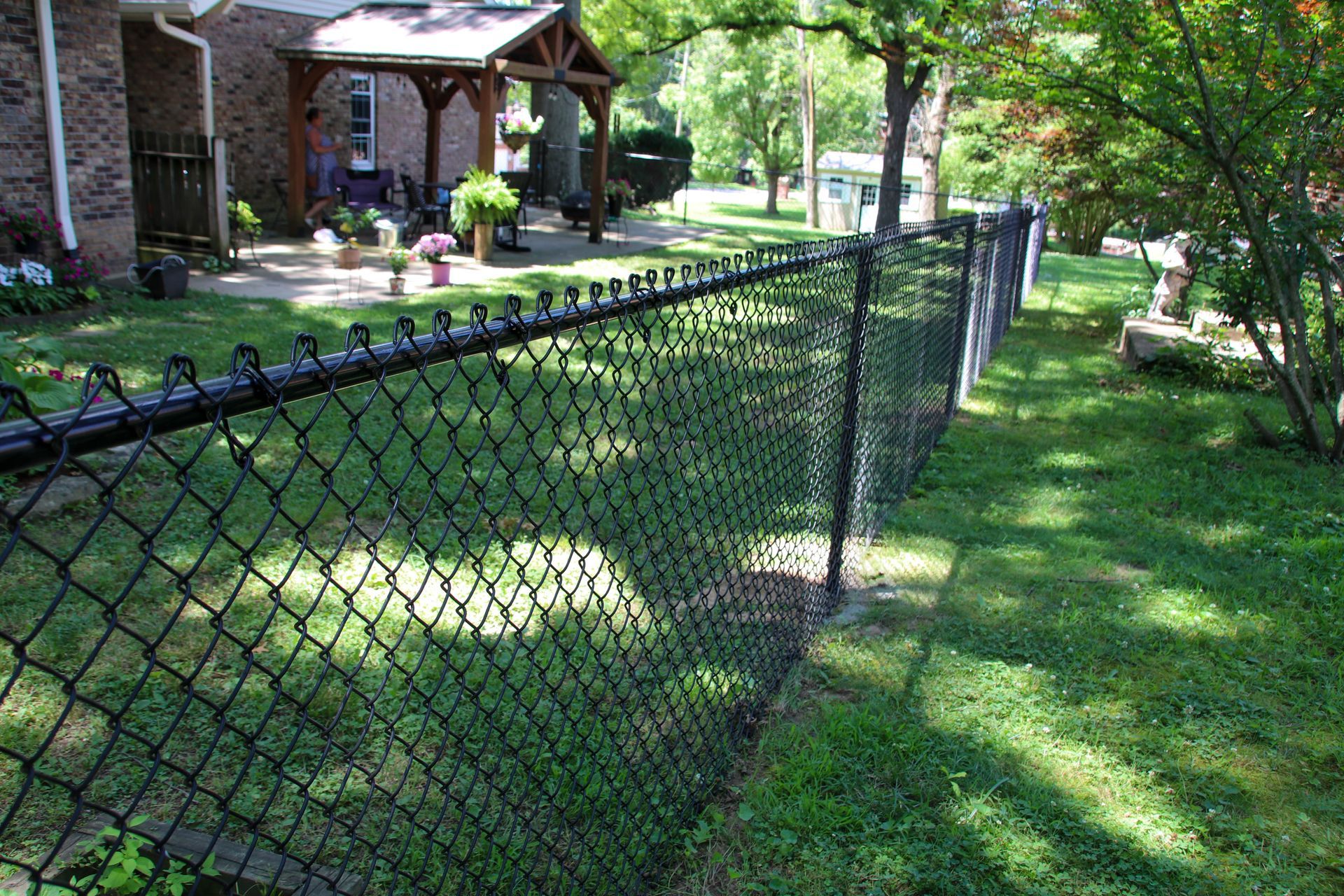 Black chain-link fence bordering a grassy yard, with a house and porch in the background.