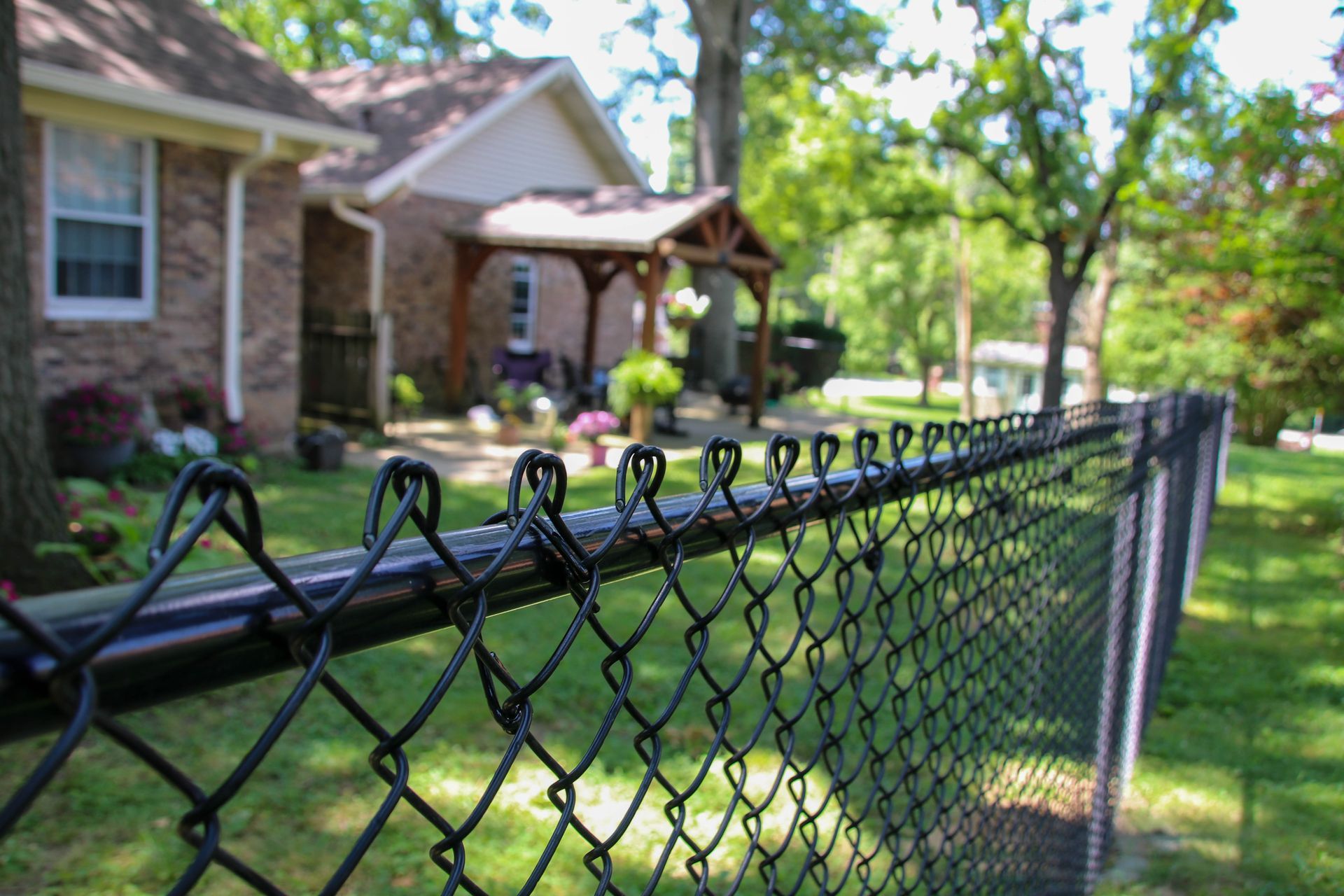 Black chain-link fence in front of a brick house with a wooden porch on a sunny day.