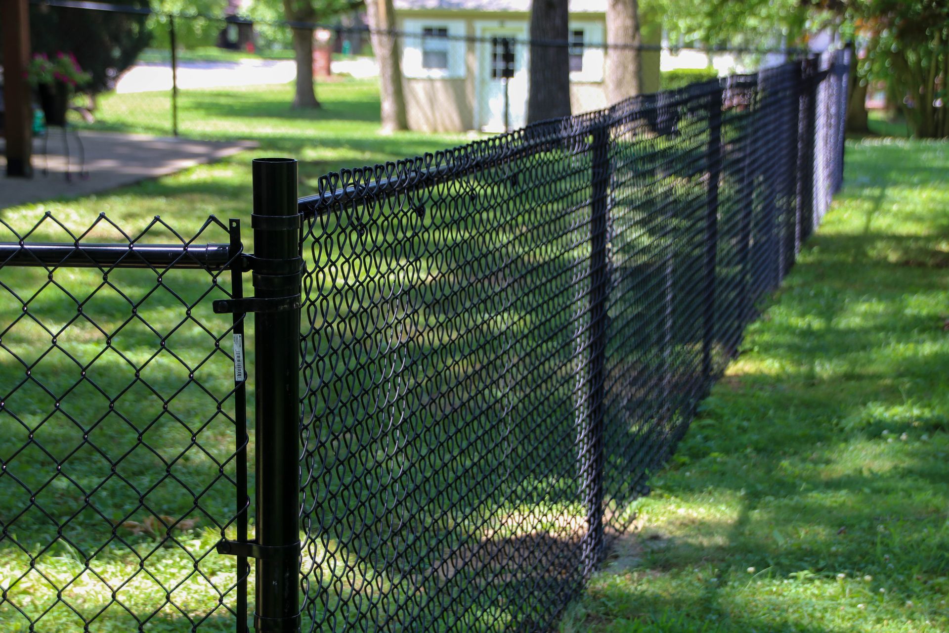 Black chain-link fence in a grassy yard, with a glimpse of a house in the background.