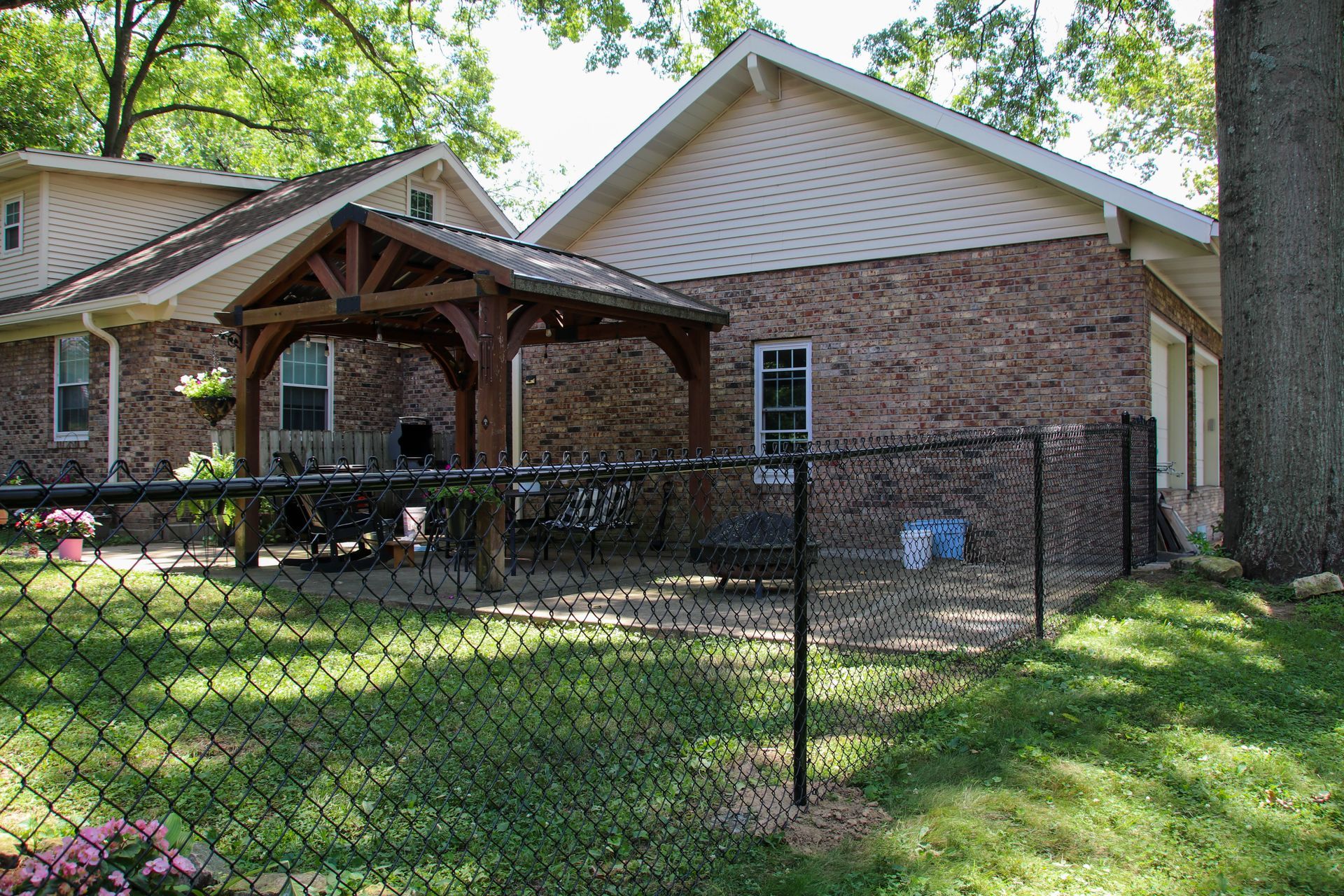 Backyard with brick house, wooden gazebo, and chain-link fence.