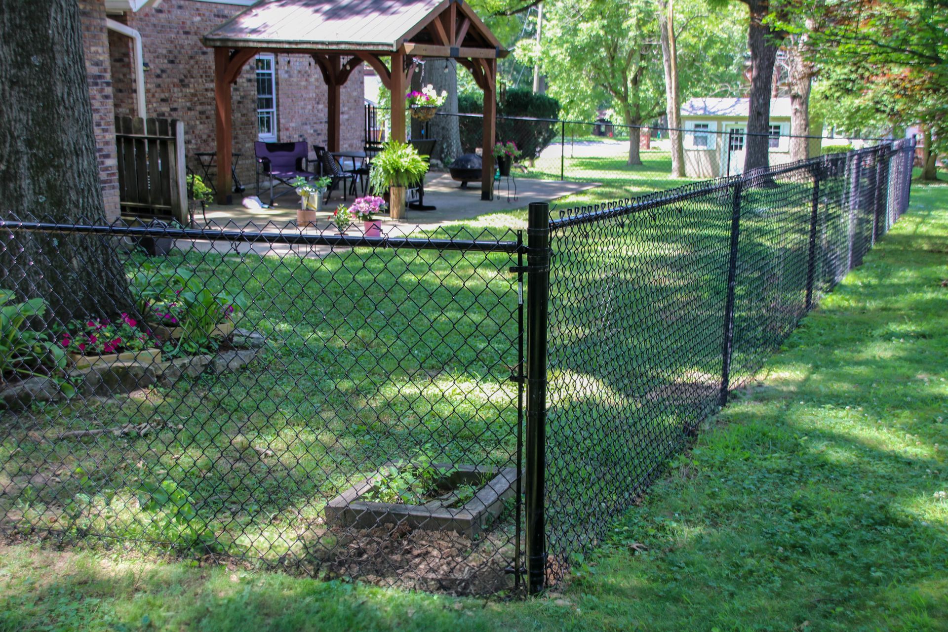 Black chain-link fence in a grassy yard, with a brick house and arbor in the background.