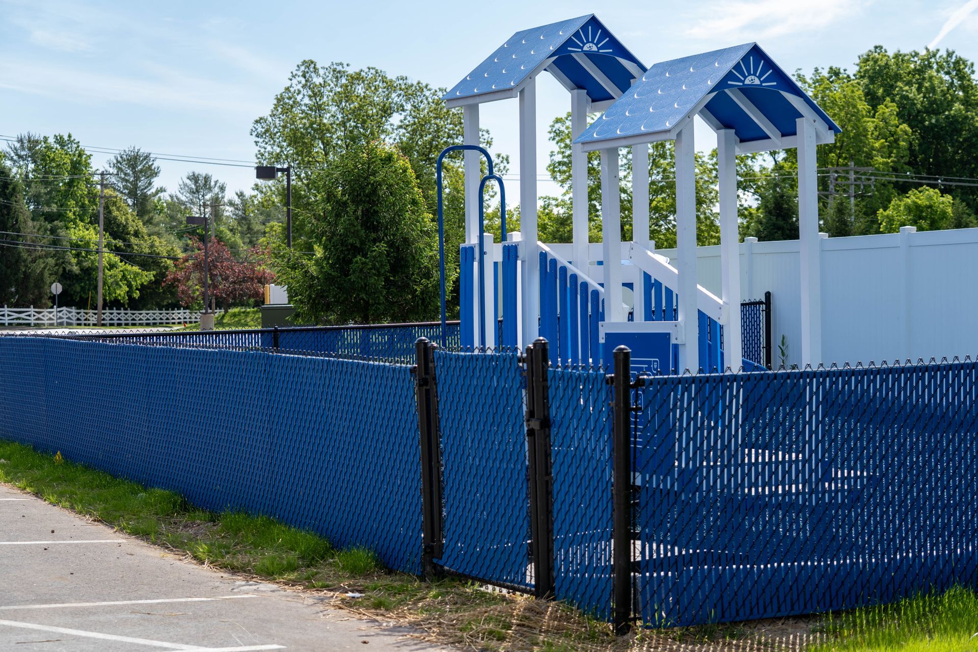 Blue fenced playground with white and blue structures, in an outdoor setting on a sunny day.