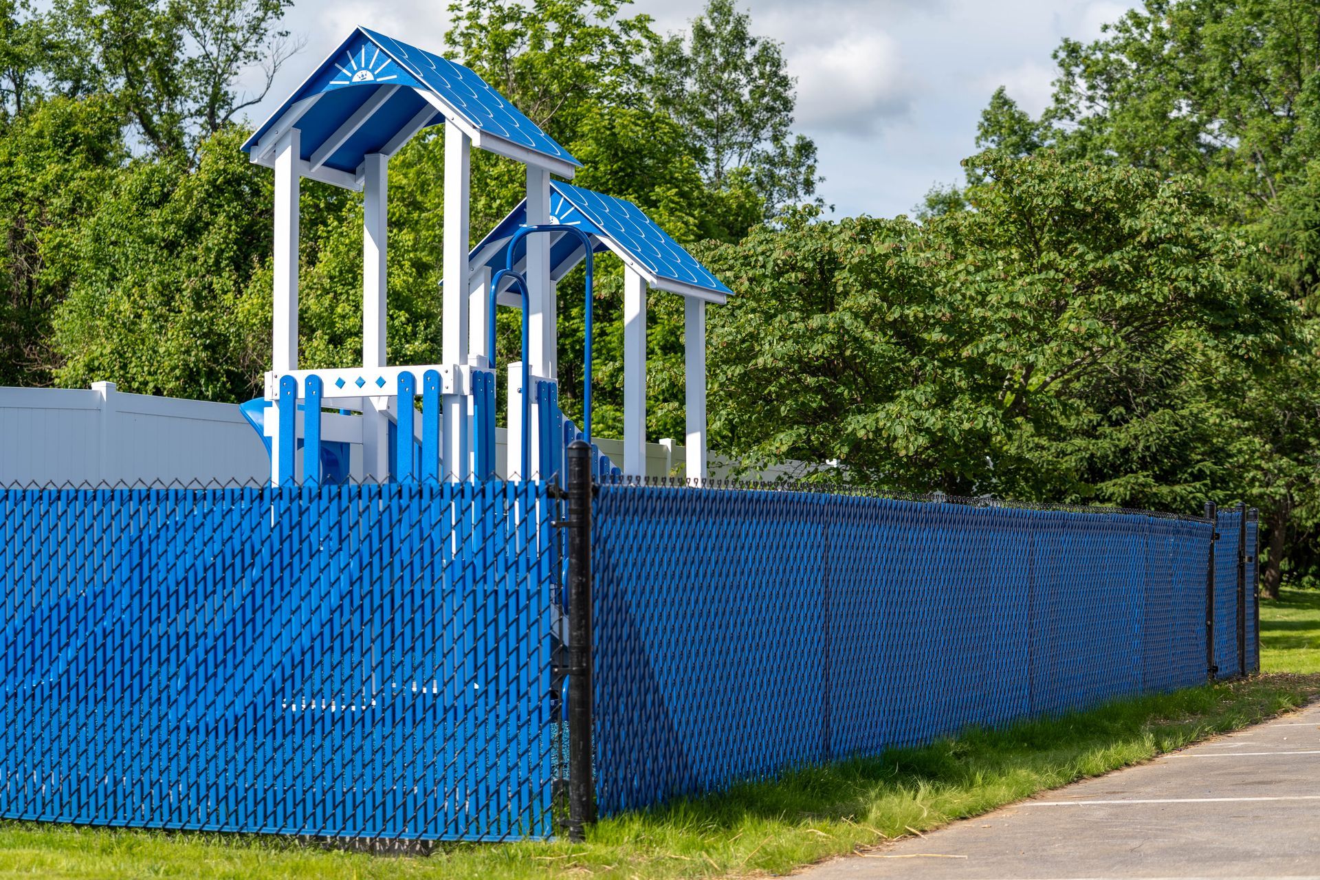 Blue fenced playground with play structure and trees.
