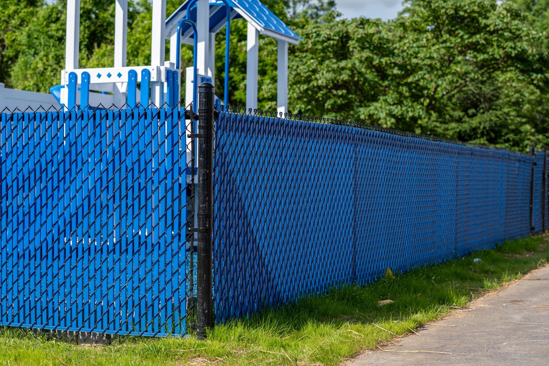 Blue privacy slats in a chain-link fence surround a playground.