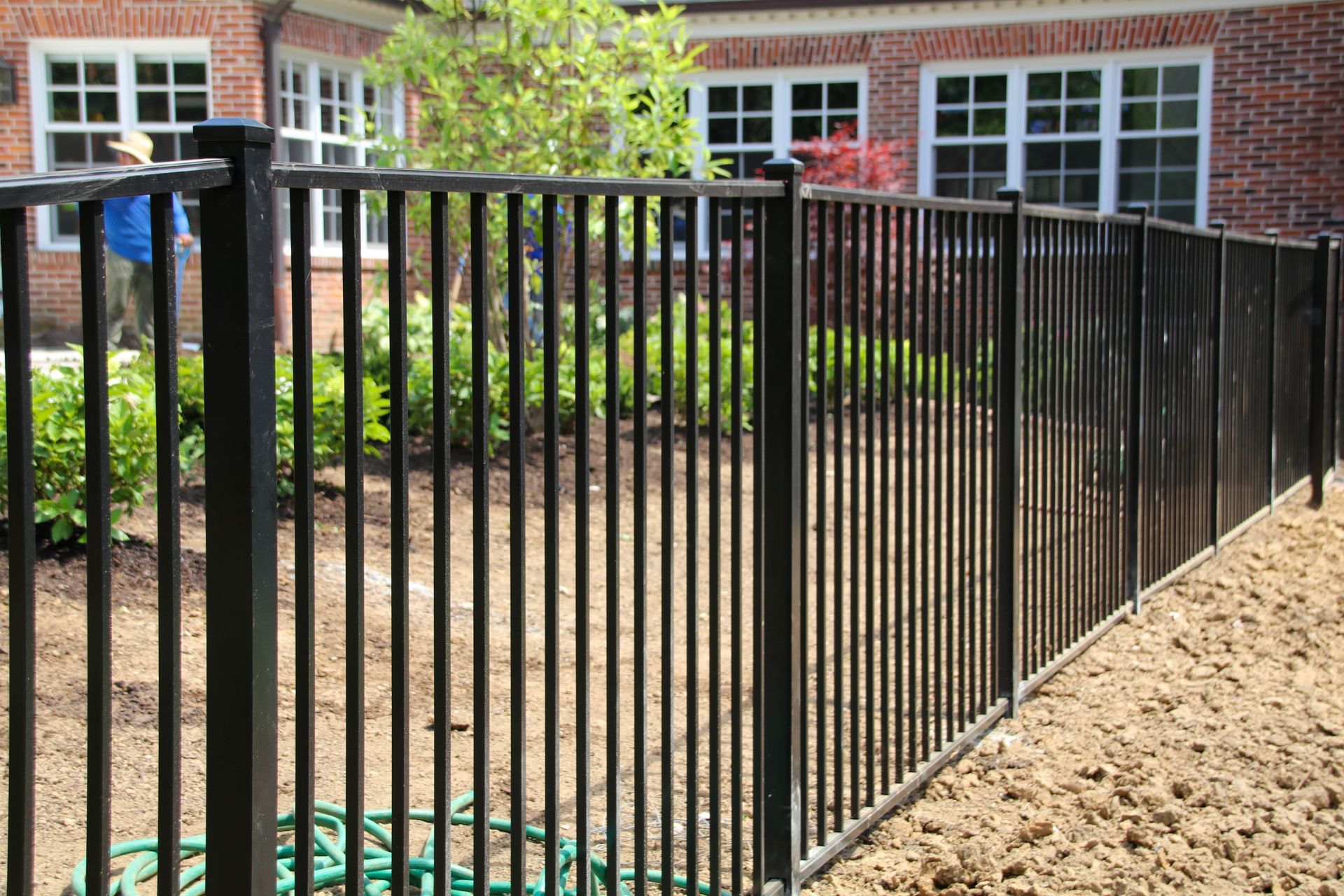Black metal fence in front of a brick building and a green yard with plants.