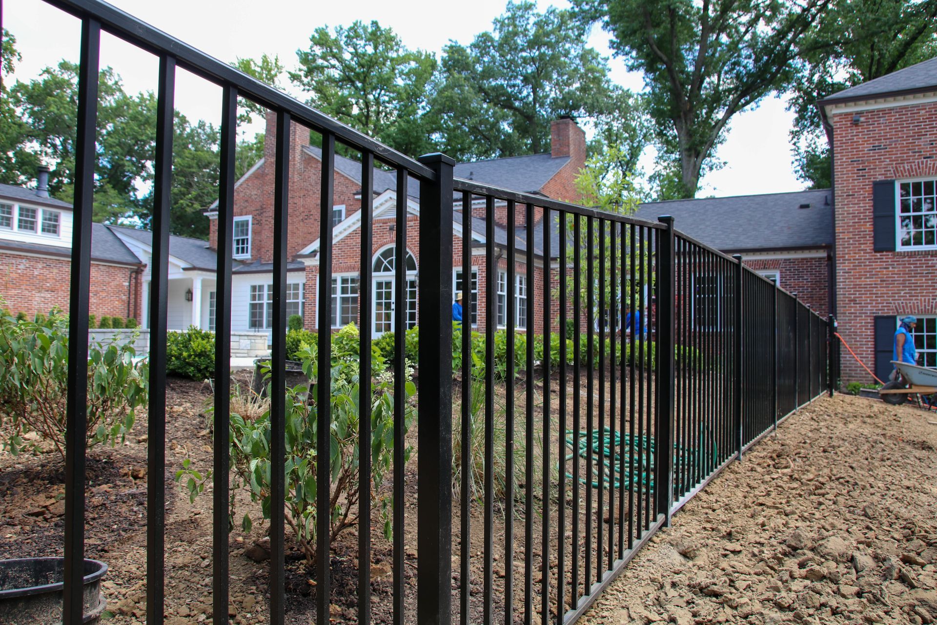 Black metal fence along a property, with a brick house visible in the background.