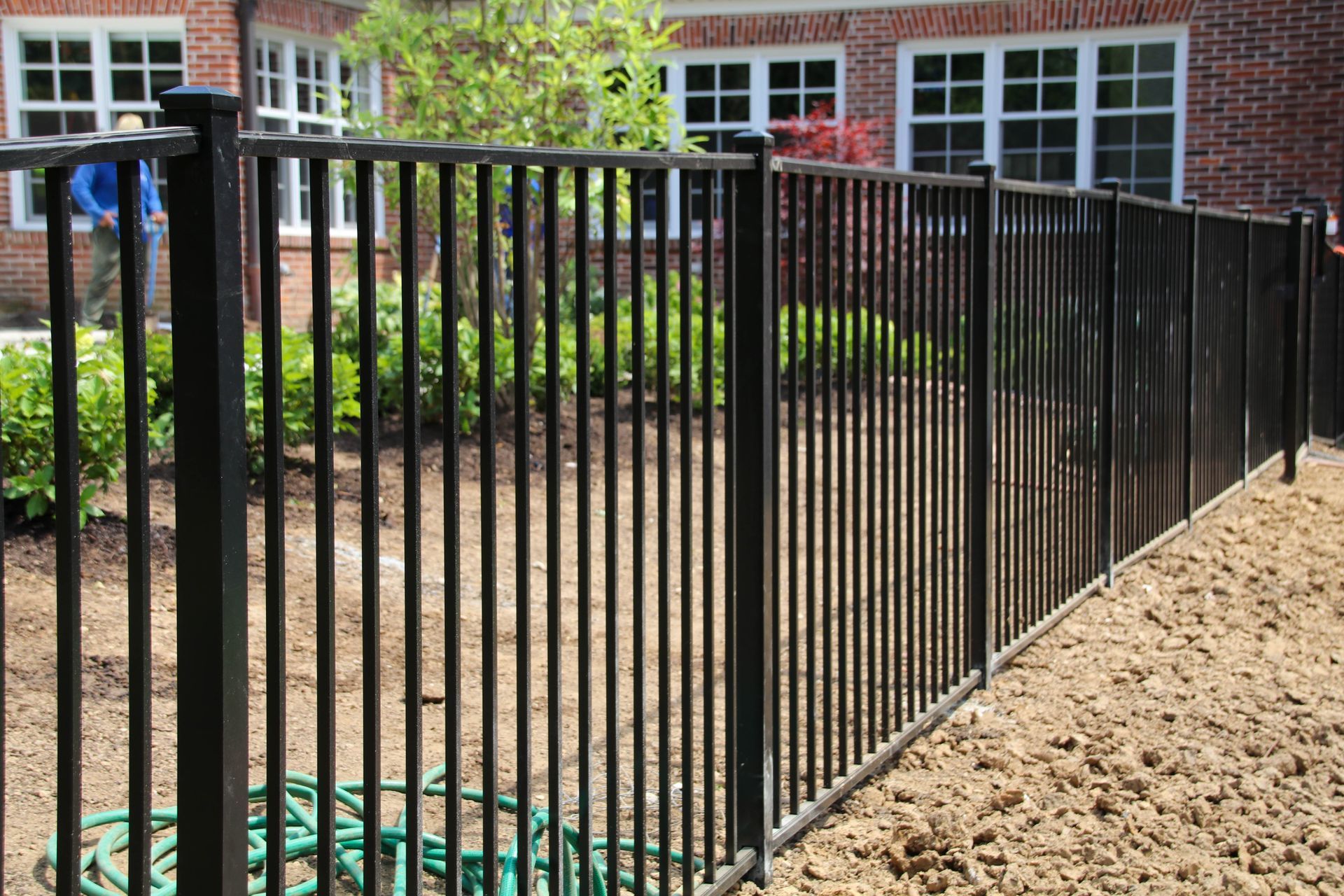 Black metal fence along a yard with a red brick building in the background.