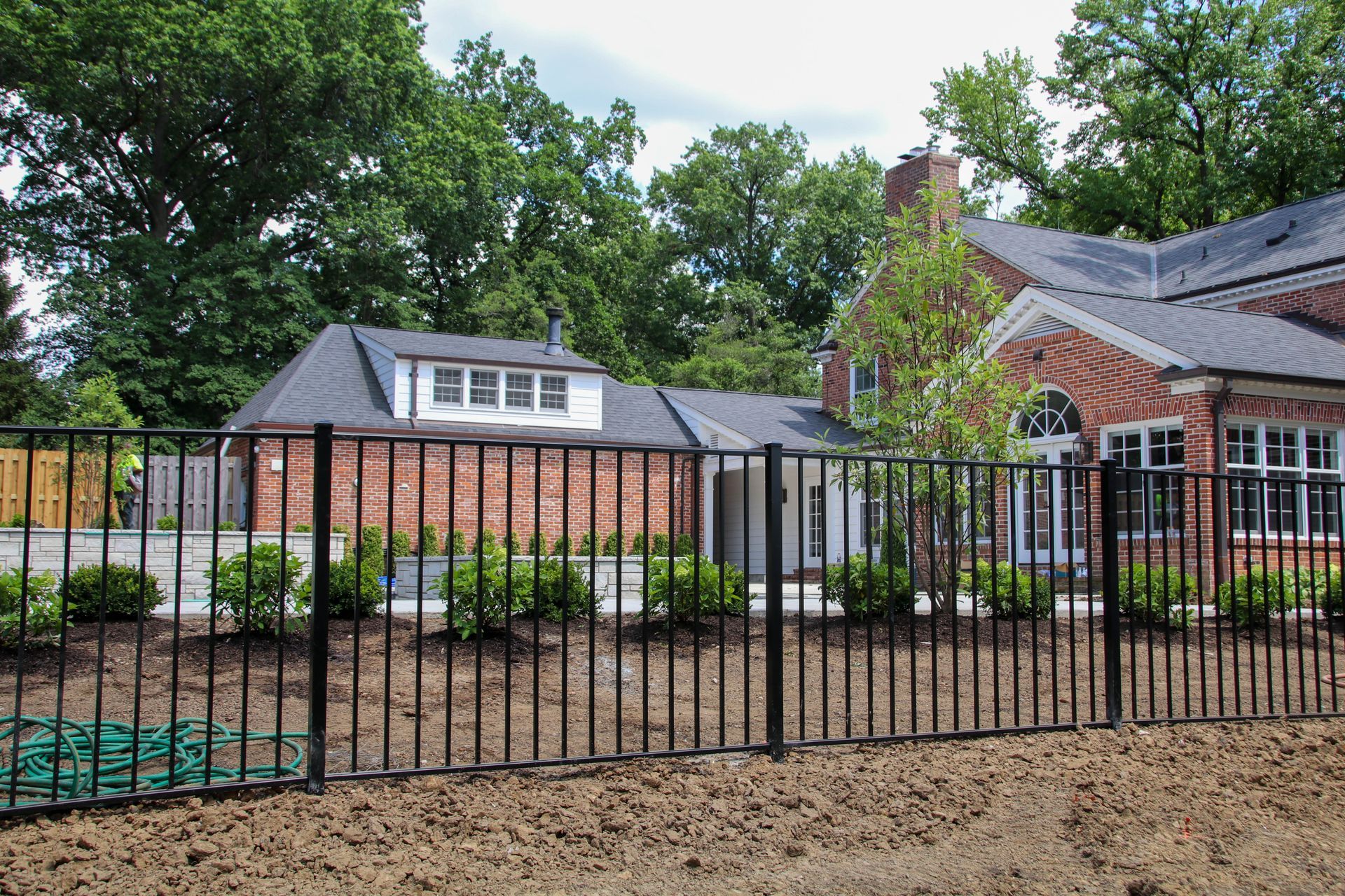 Black metal fence in front of a brick house with a green hose on the ground.