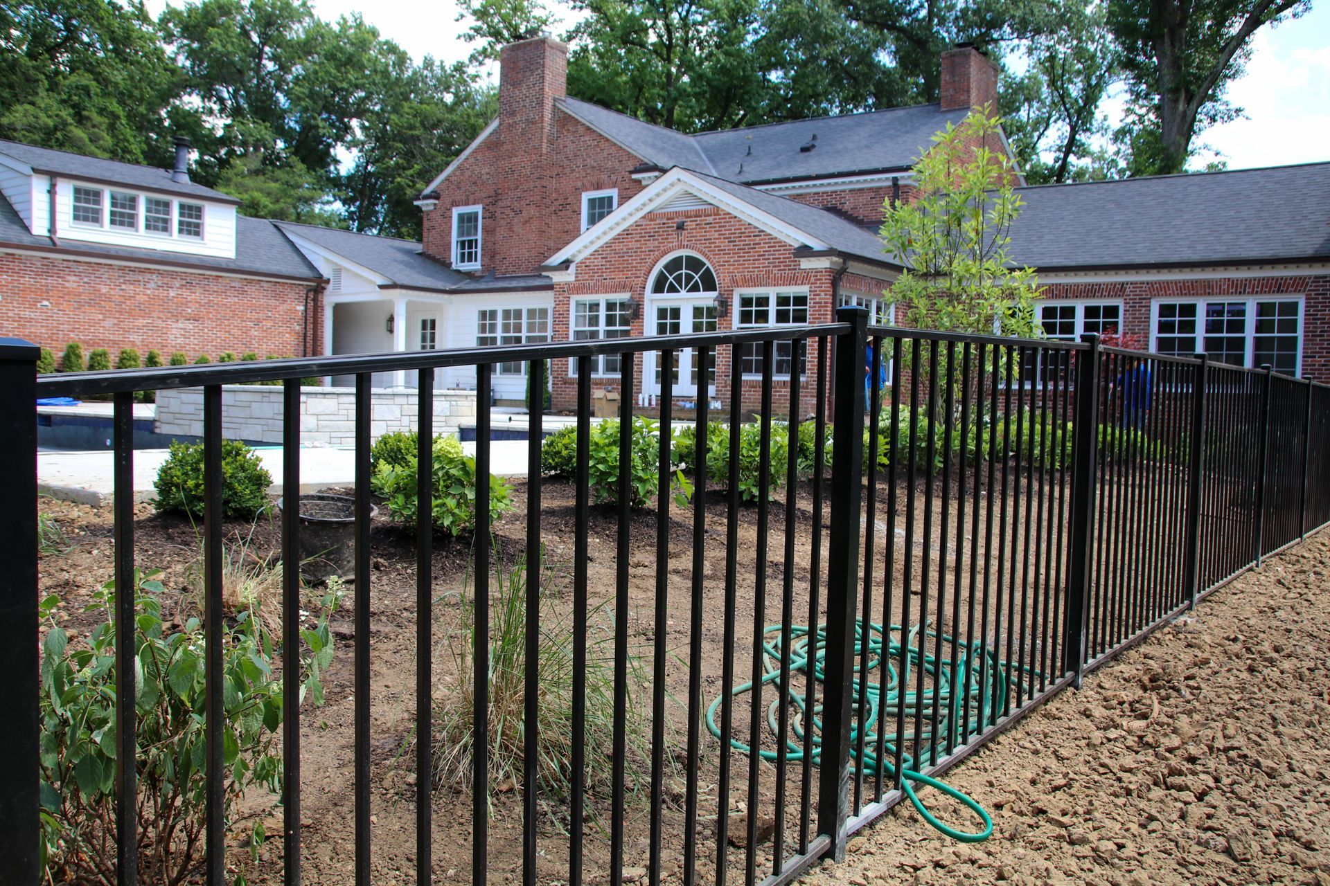 Black metal fence in front of a brick building with a swimming pool and landscaping.