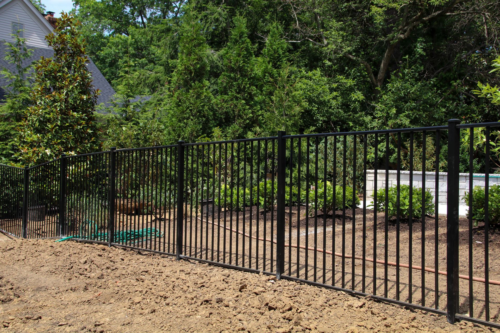 Black metal fence in a yard with trees and house in the background.