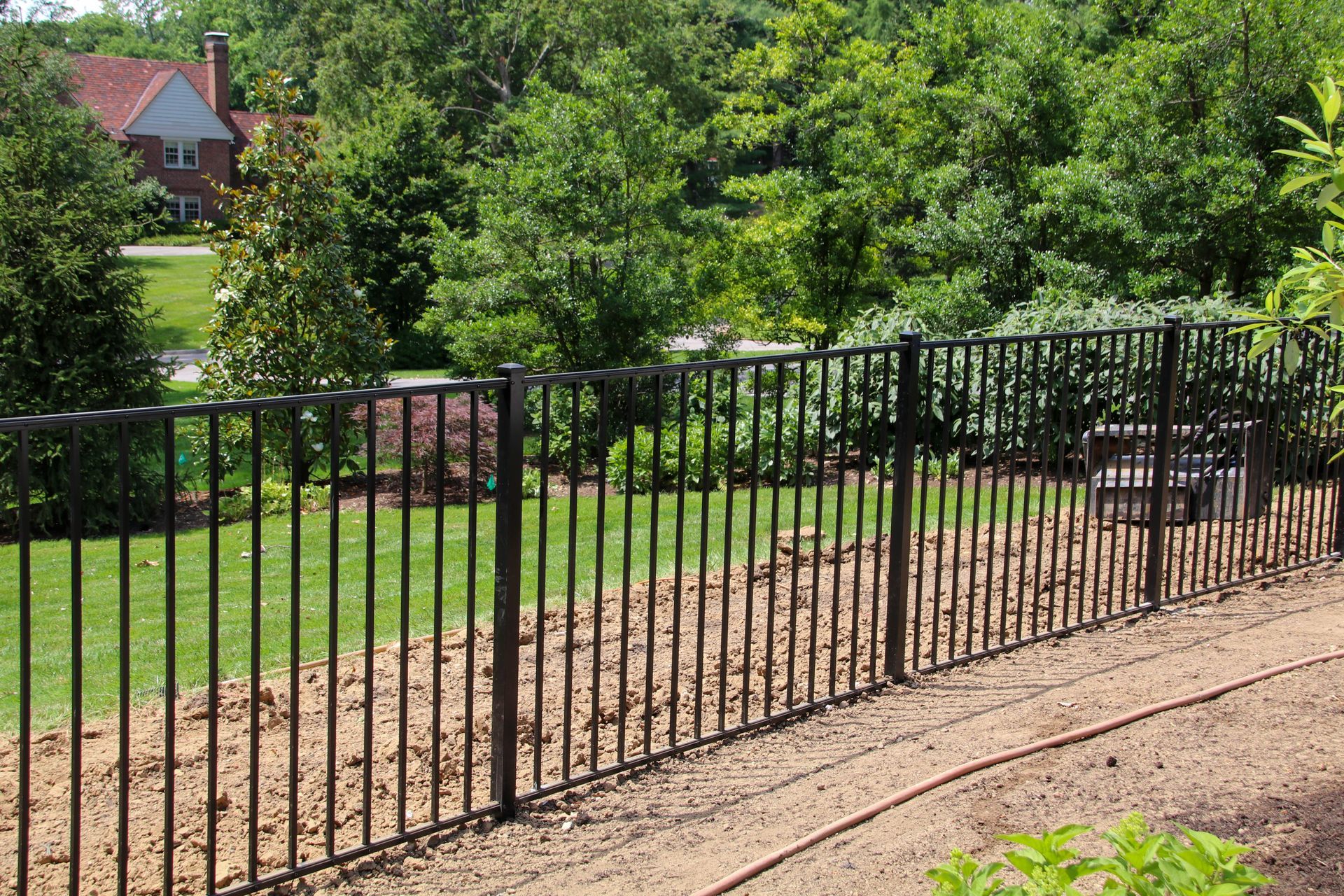 Black metal fence in a yard with grass and trees.