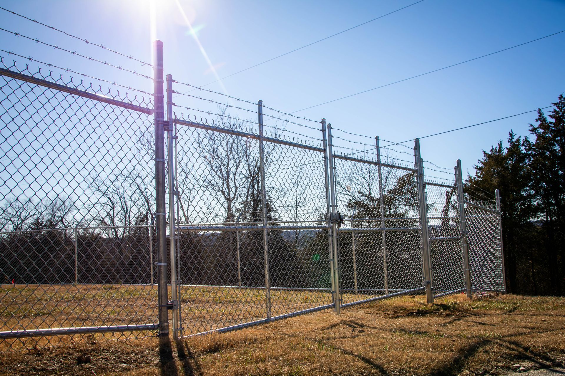 Chain-link fence with barbed wire on top, under a bright sun.