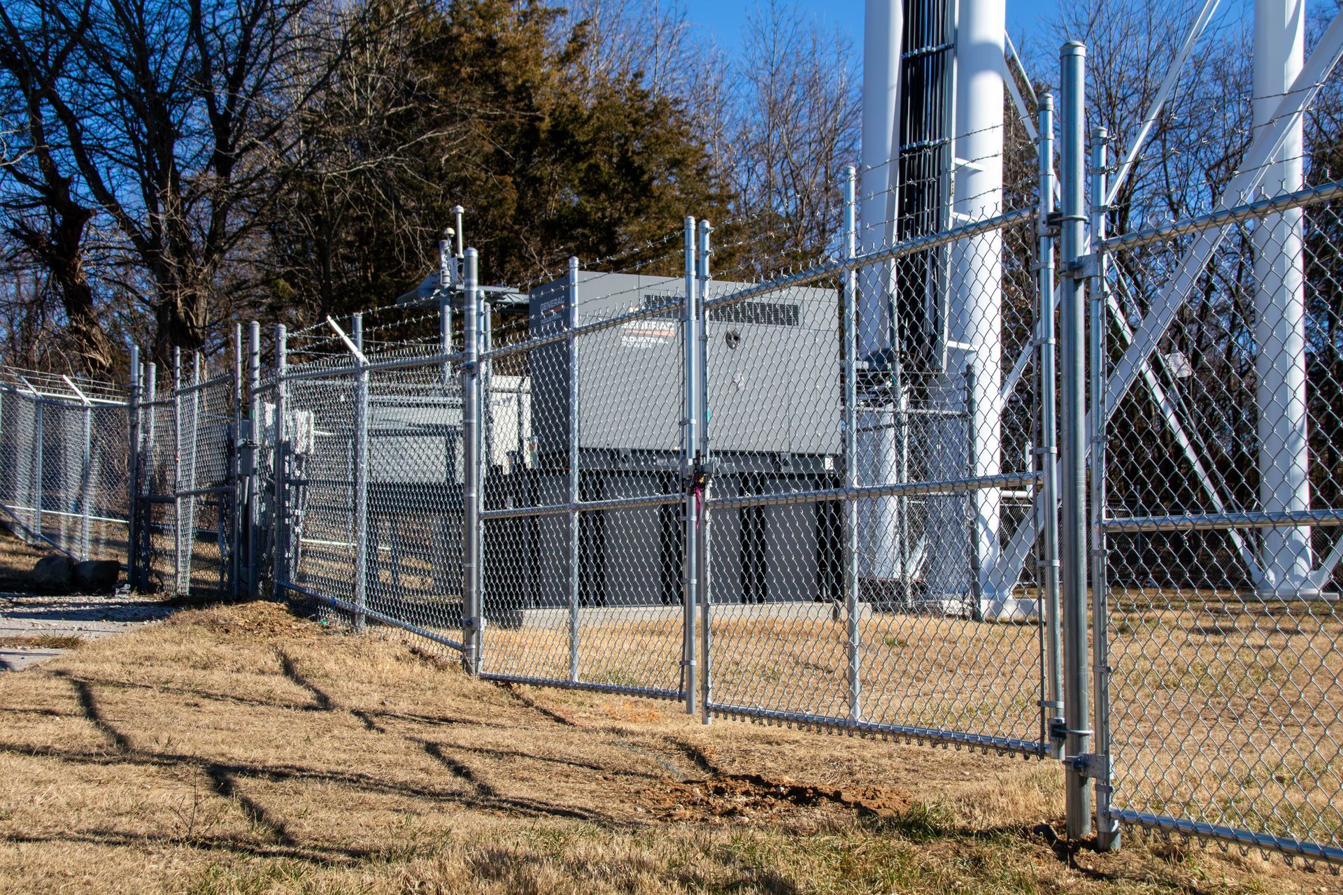 Fenced utility building with a radio tower in the background, on a sunny day.