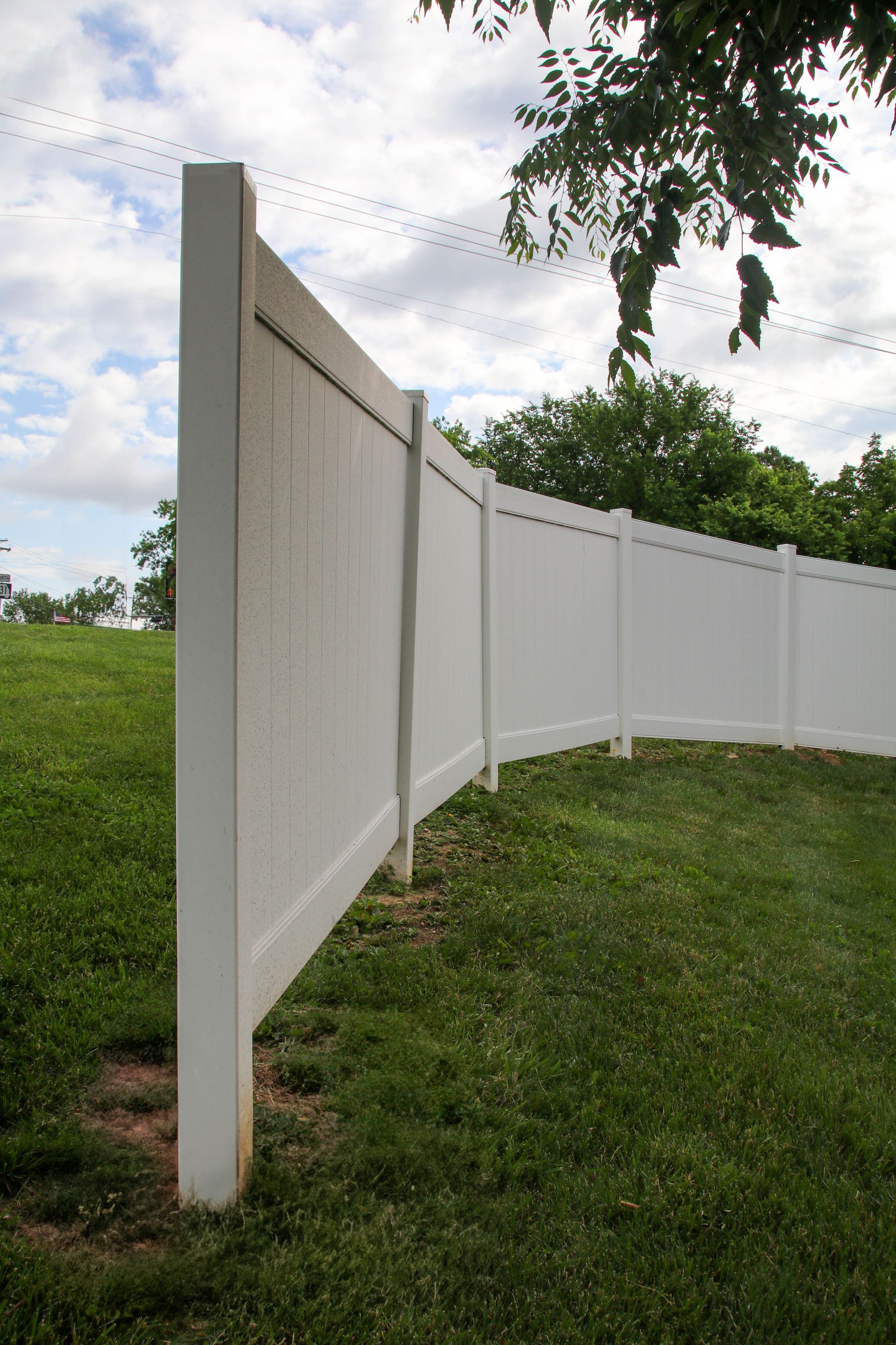 White vinyl fence on a grassy hill, under a cloudy sky.