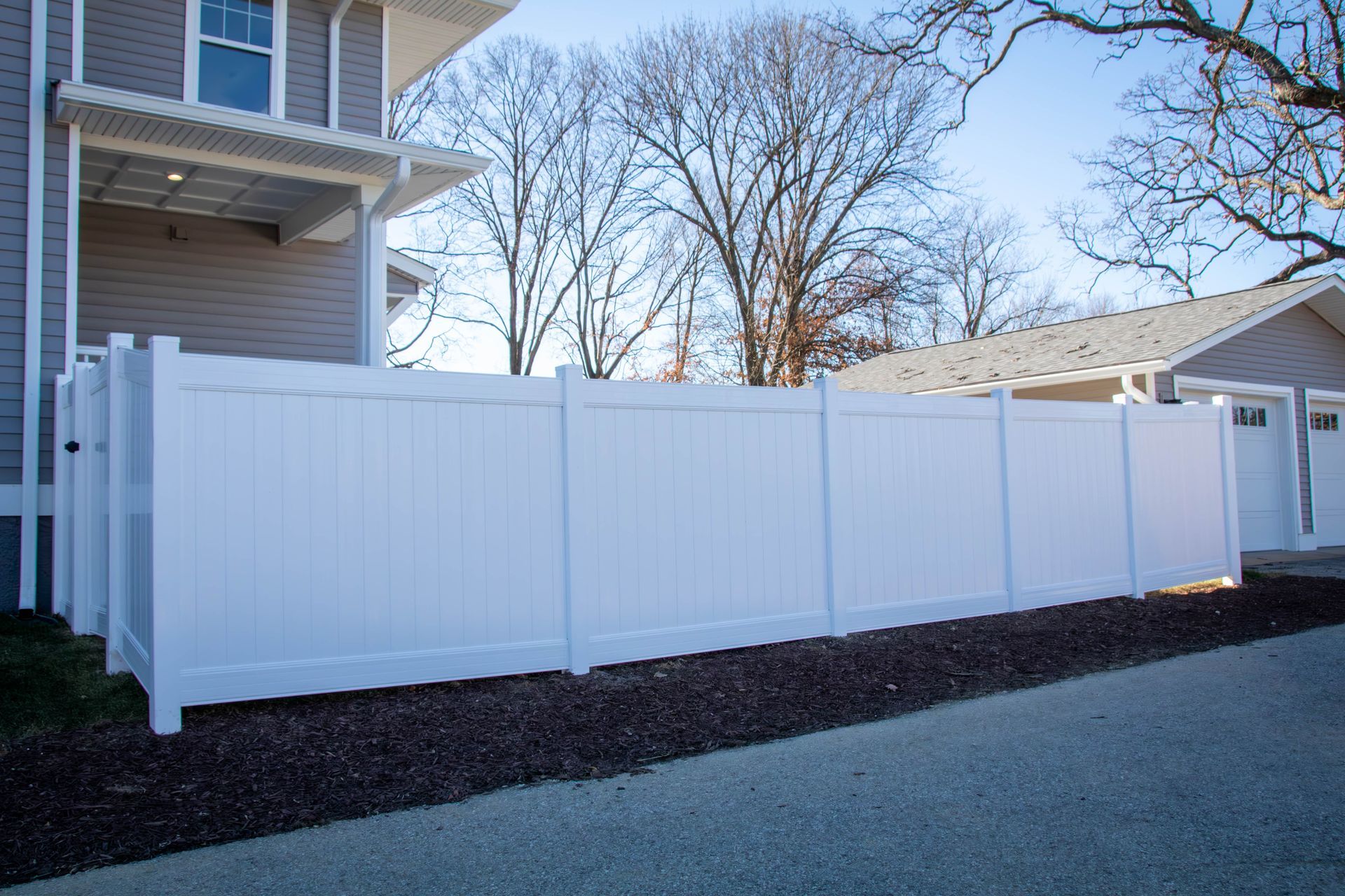 White vinyl fence alongside a light-colored house and garage on a sunny day.