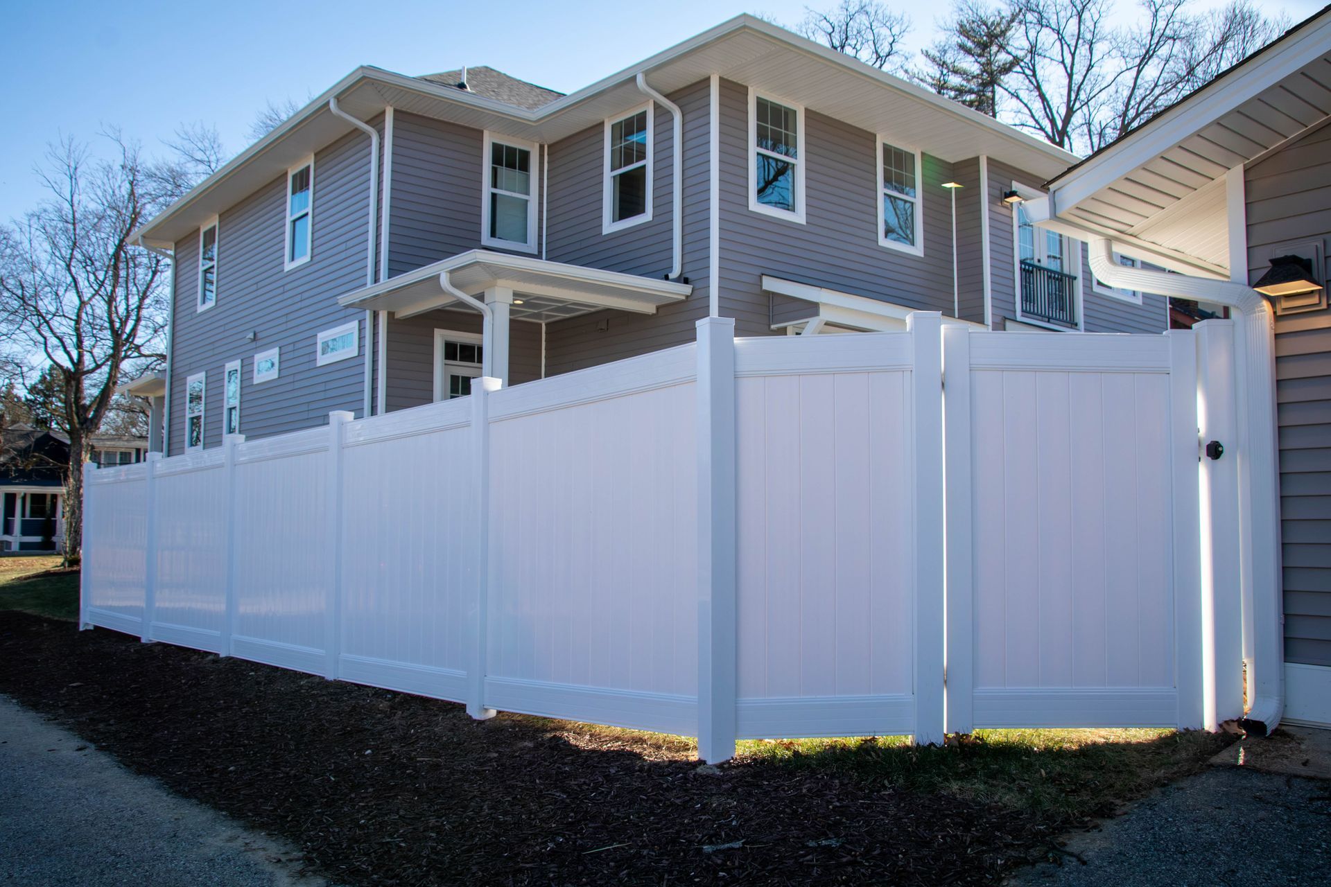 White vinyl fence surrounds a two-story gray house.